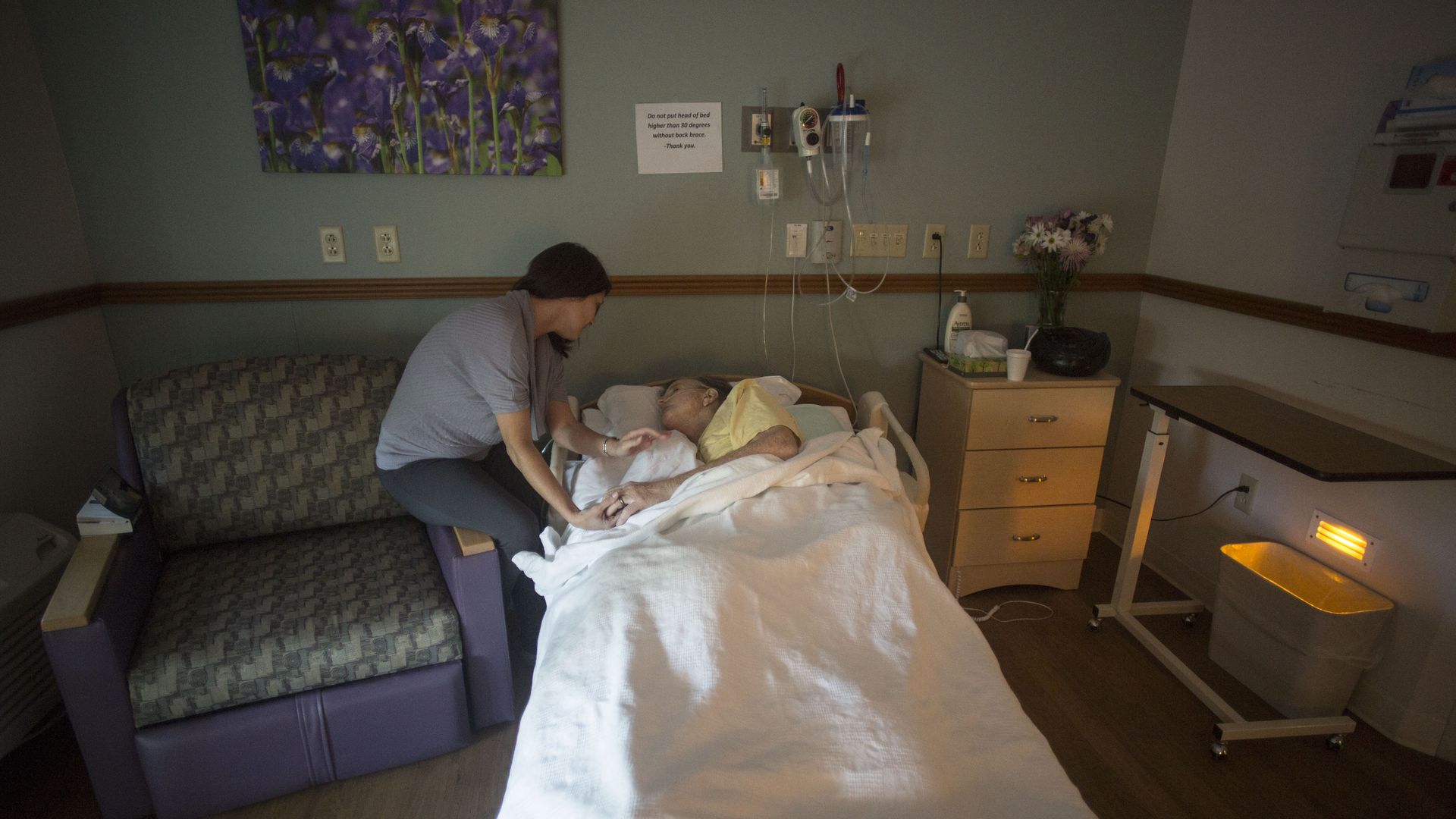 A wife comforts her husband in a hospice room.