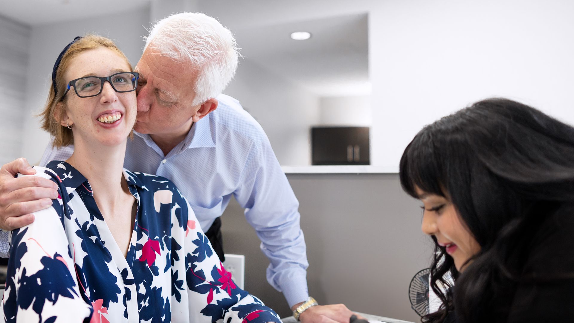 A man kisses a young woman on the cheek while another woman services her nails.
