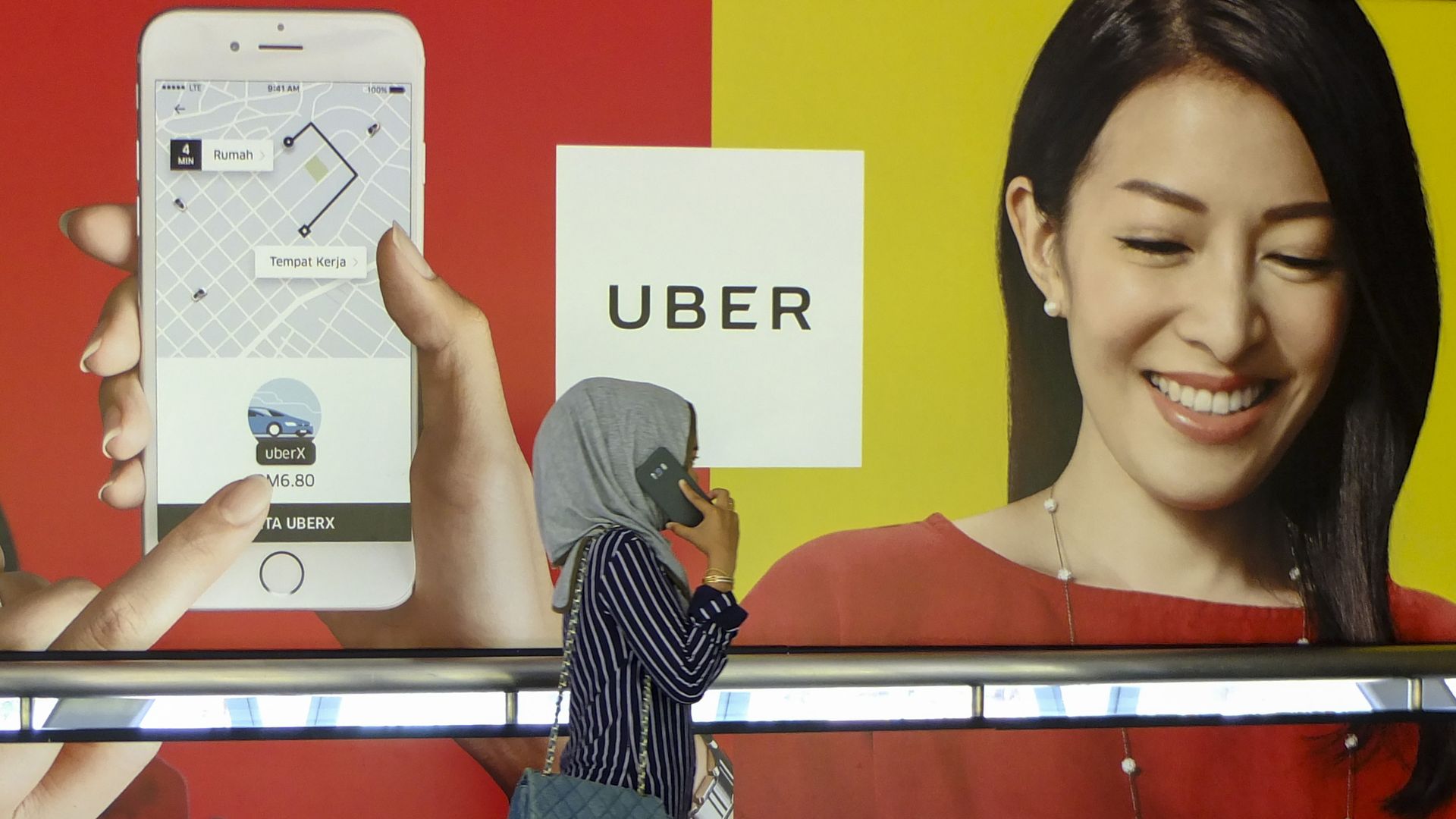 A woman on the phone walks by an Uber advertisement. 