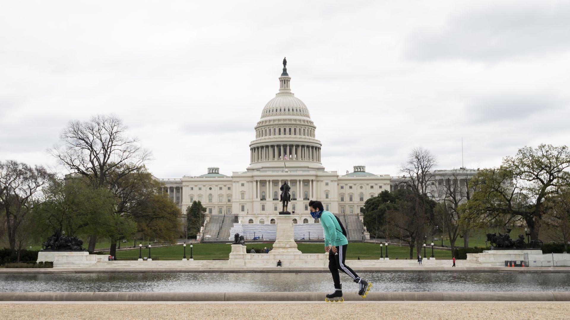 A man wearing a bandana as a face mask roller blades past the U.S. Capitol building