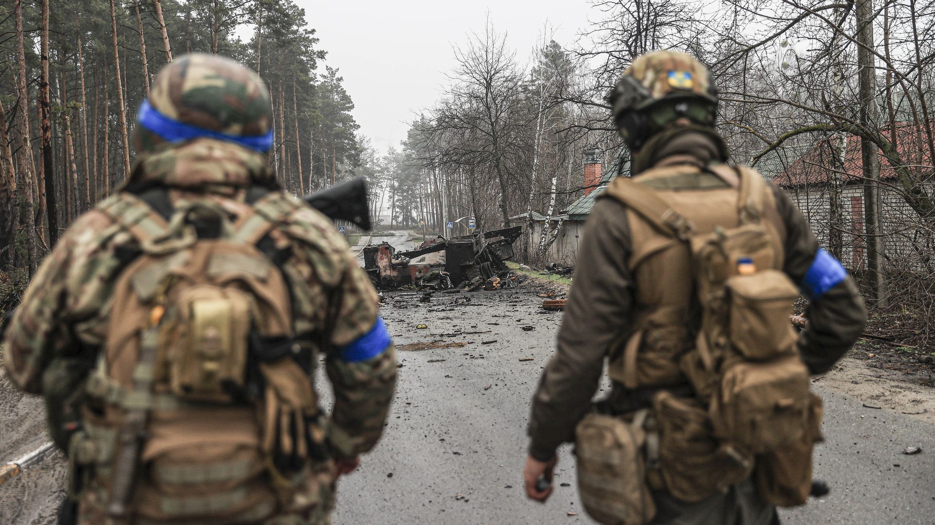 Photo of two uniformed Ukrainian soldiers gazing upon a burned vehicle in the middle of a road