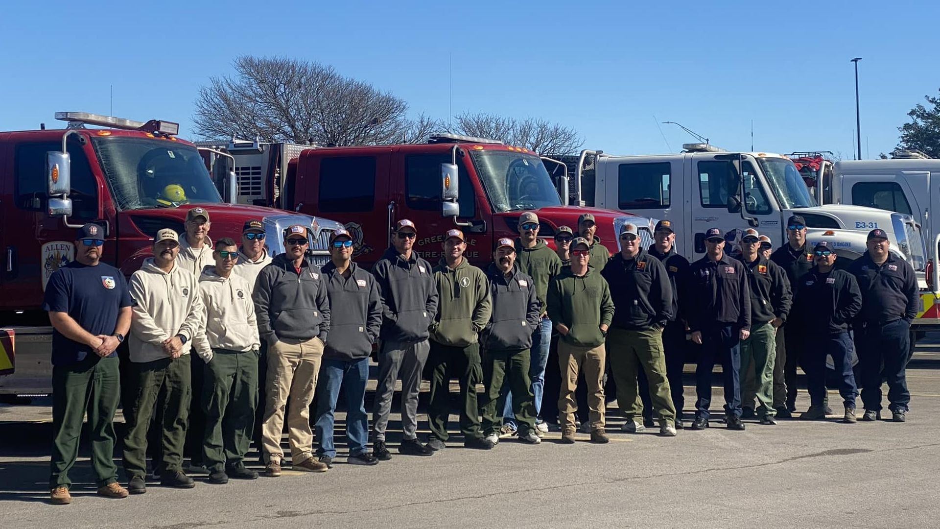 Around 20 people stand in front of fire engines