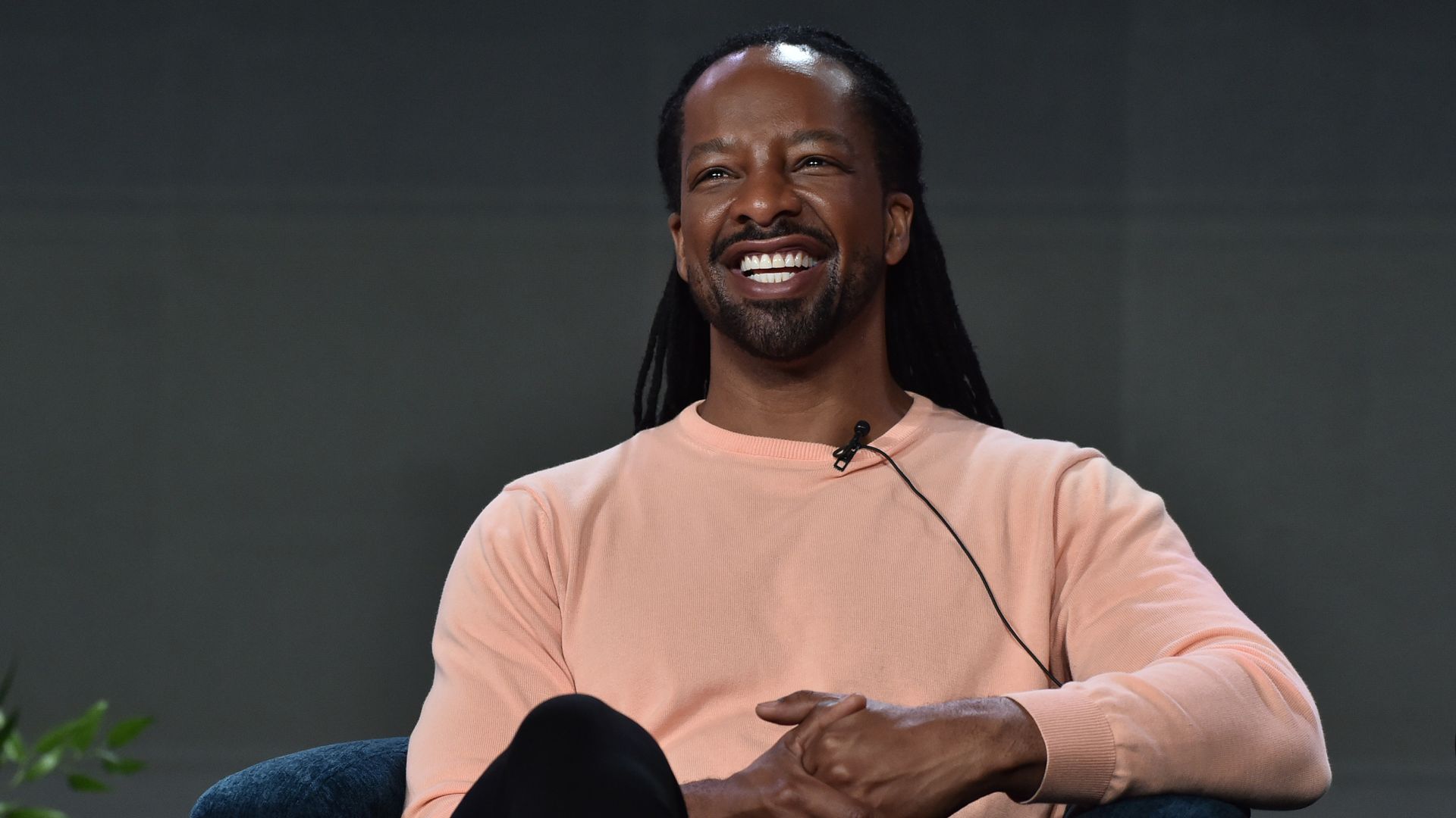 An individual wearing a salmon colored shirt smiles and laughs while being interviewed at a public event