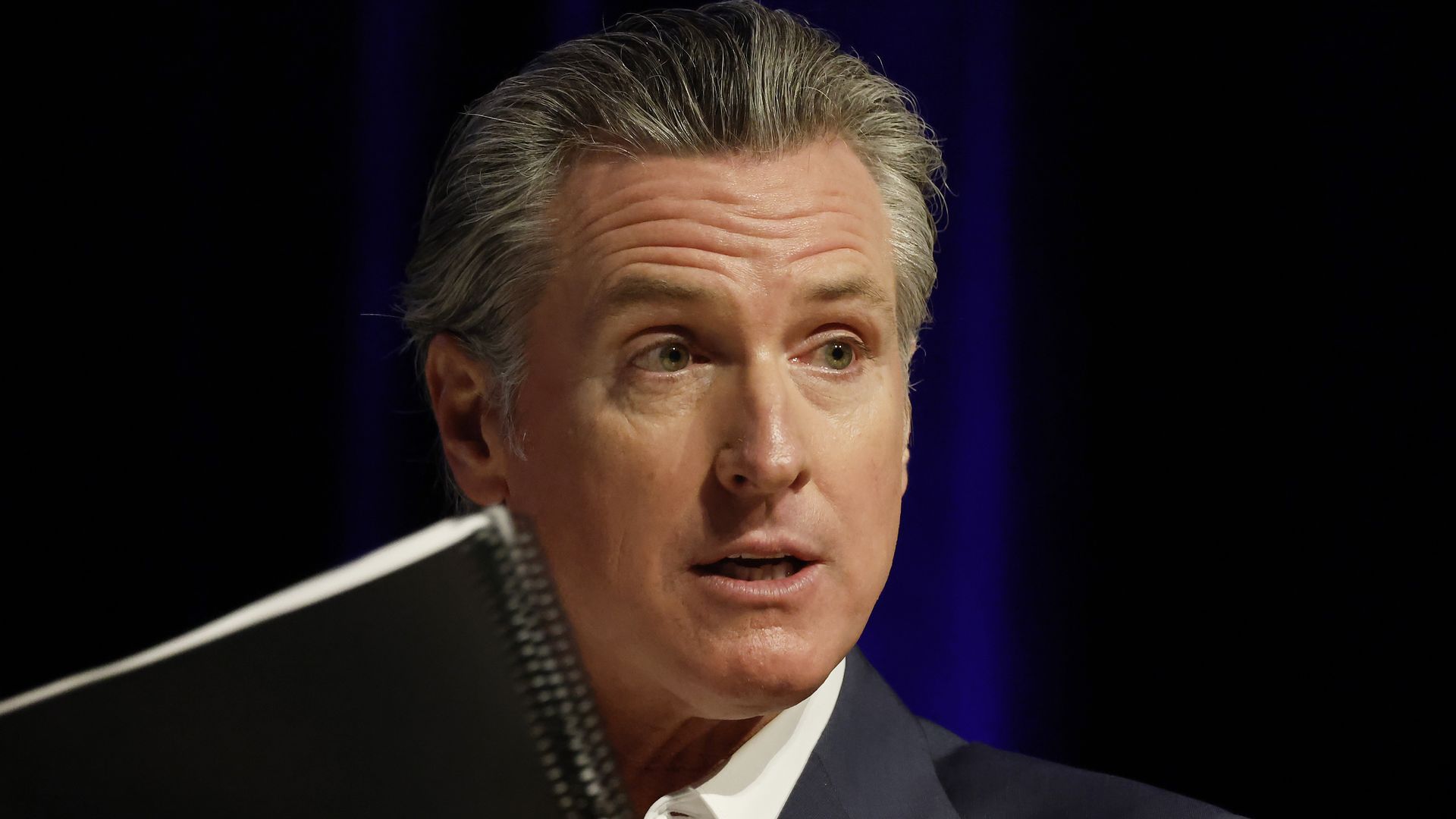 Photo of Gavin Newsom speaking with a notebook in the foreground