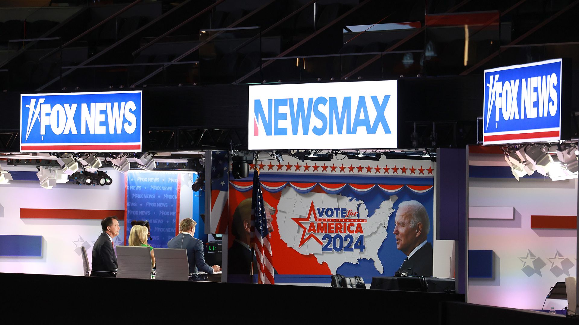 A television studio with Fox News and Newsmax banners hanging overhead.