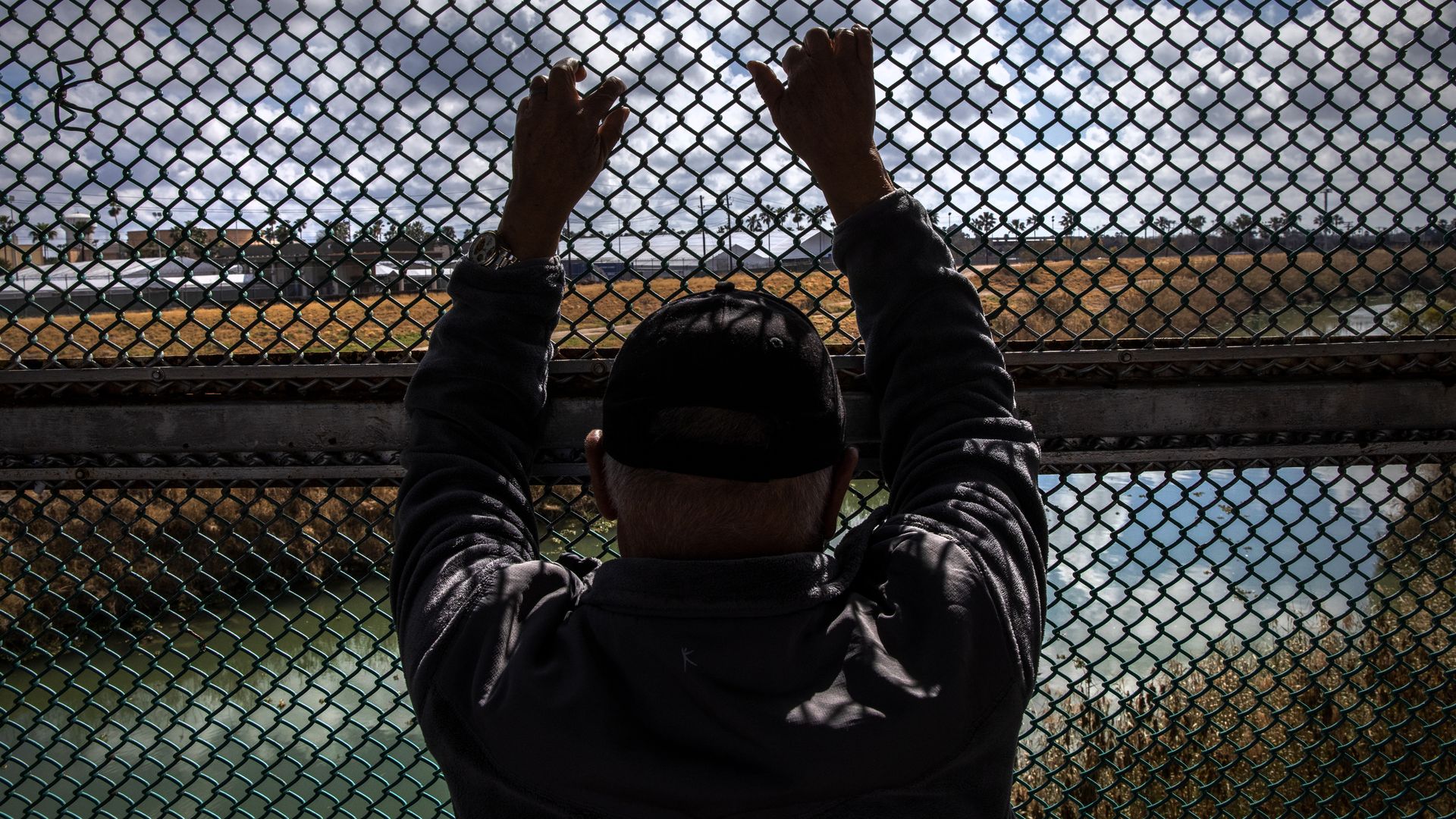 A person holds onto a chain linked fence.