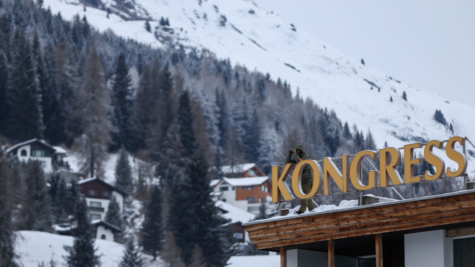 Scenic photo of a snowy mountainside with evergreens and a building in the forefront 