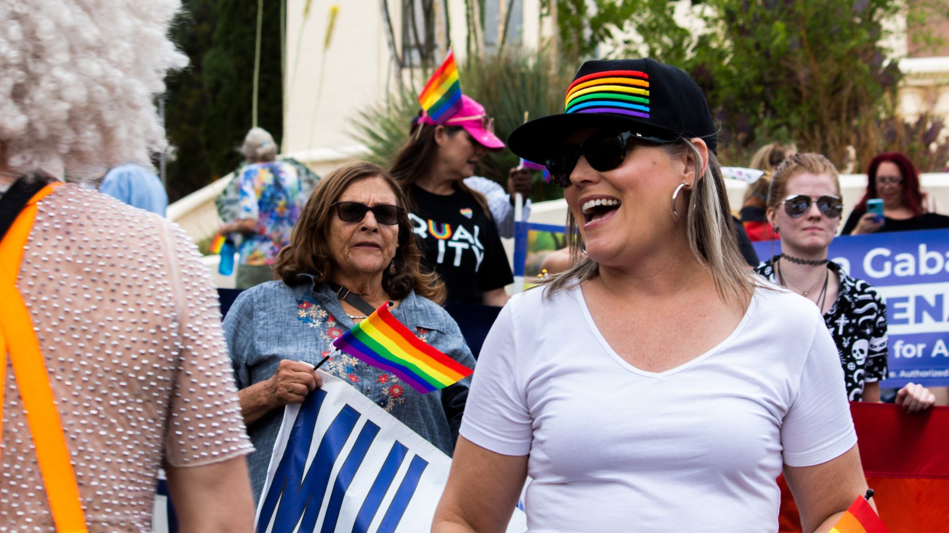 A woman smiling in a crowd wearing a hat with a rainbow.