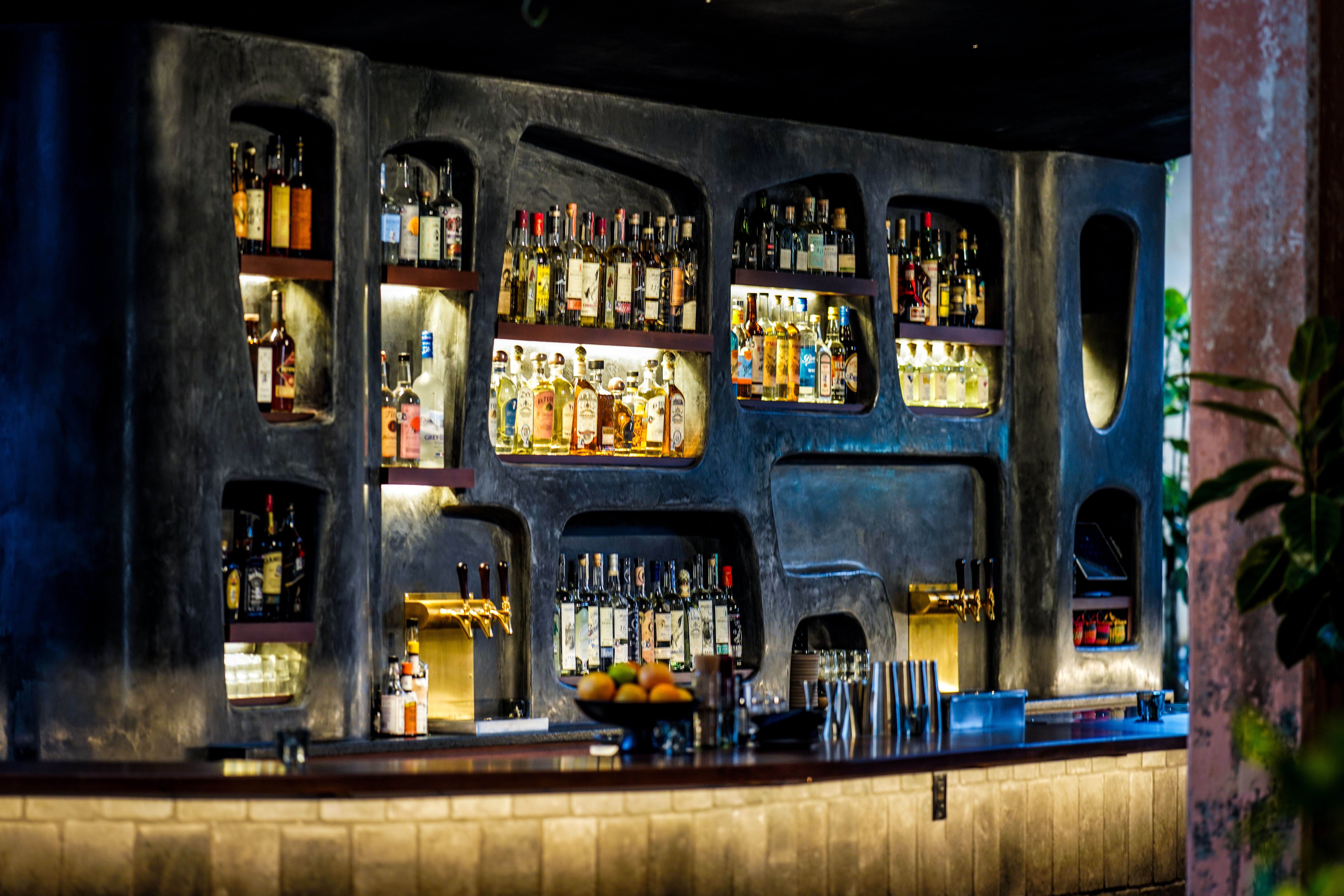 A bar carved into a black wall stocked with liquor bottles. 