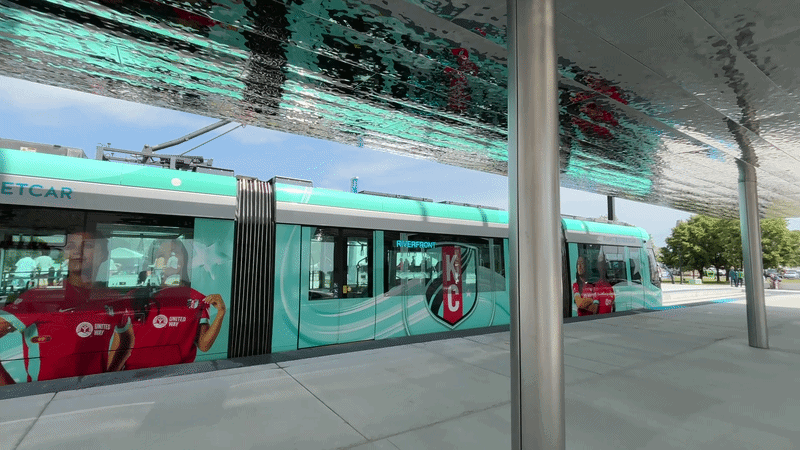 Gif shows the reflective underside of CPKC Pavilion, part of the new KC Streetcar stop down at Berkley Riverfront. A teal KC Current-themed streetcar sits on the tracks and its reflection is visible in the pavilion's reflective canopy.