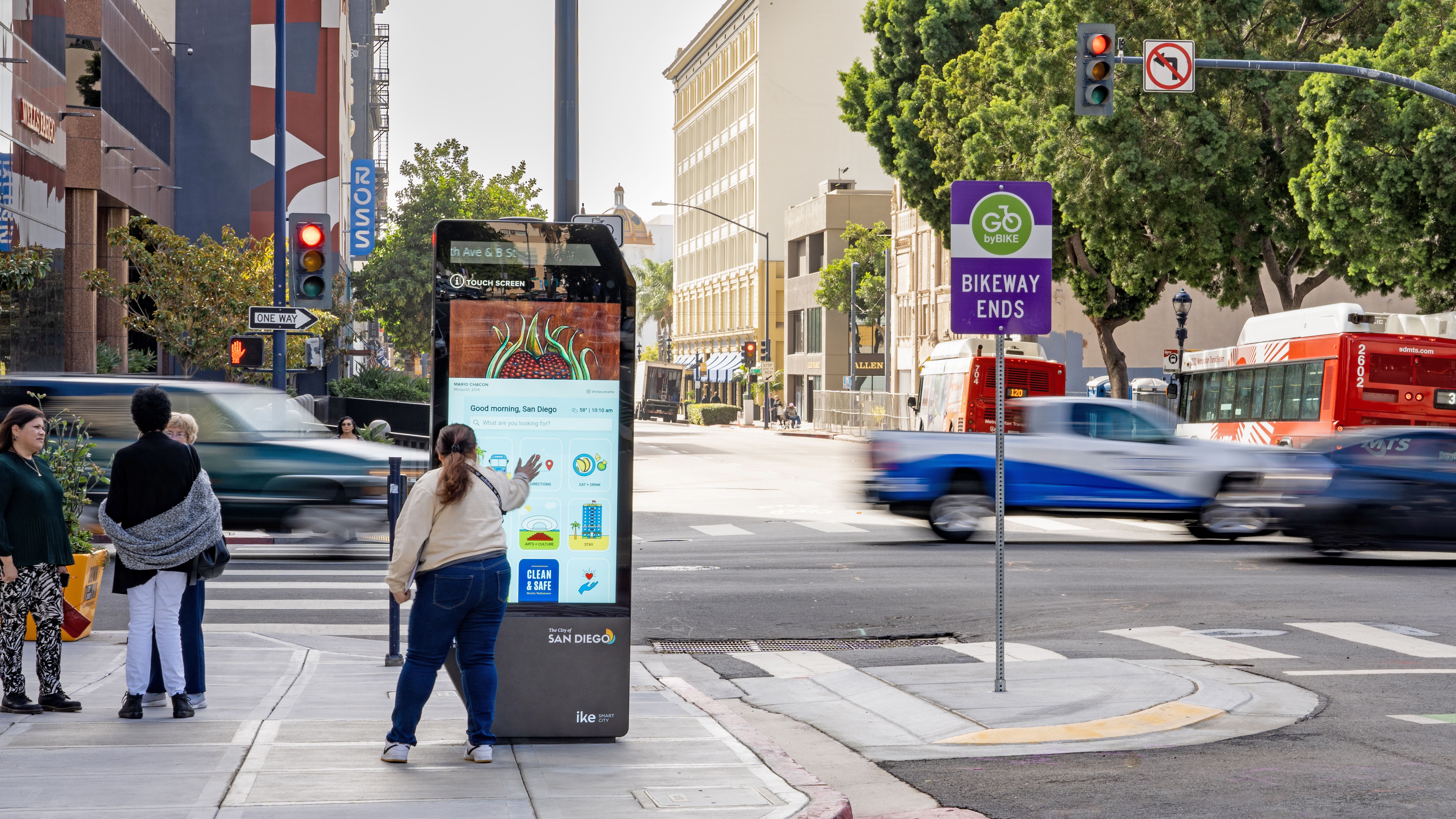 A person uses a touch-screen digital kiosk on a sidewalk in San Diego as cars drive by.