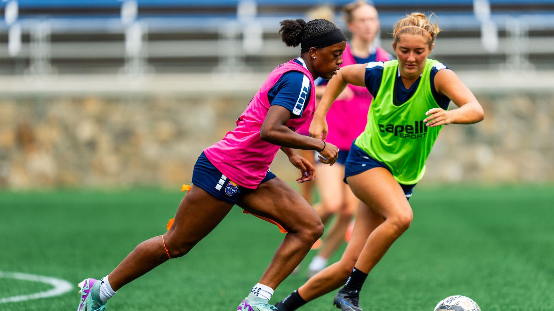Two female soccer players kicking around a soccer ball. 