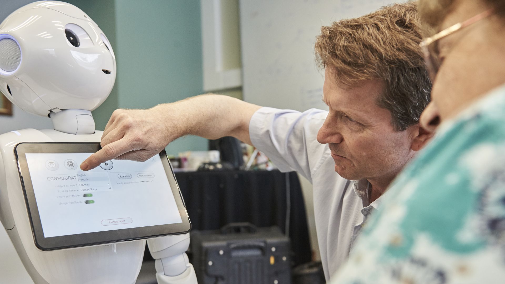 a white robot with a touch screen and a man using the touch screen