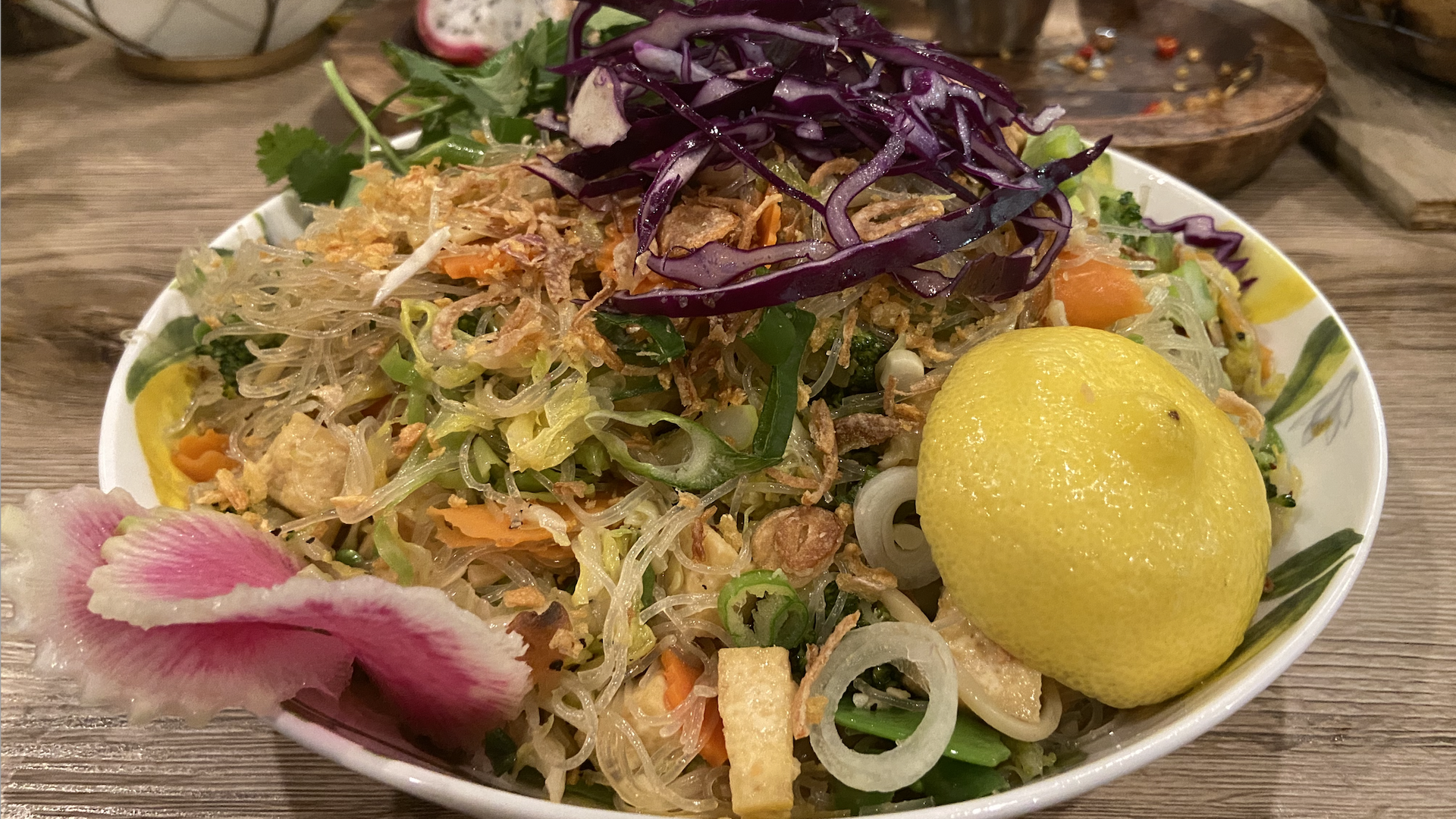 A colorful serving of pancit, a noodle dish covered in a lemon wedge, purple cabbage and watermelon radish