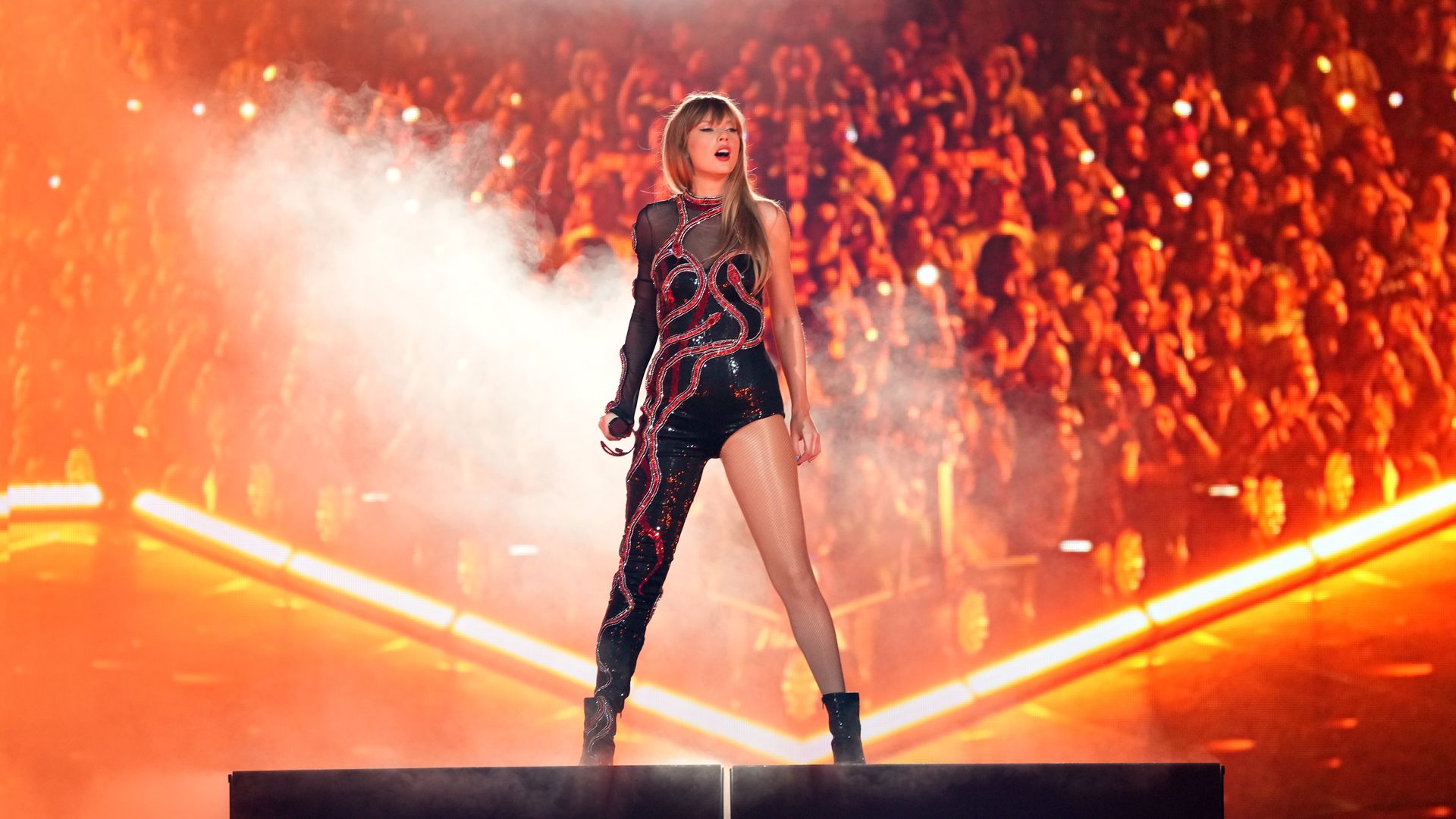 Taylor Swift stands on stage in front of a crowd. 