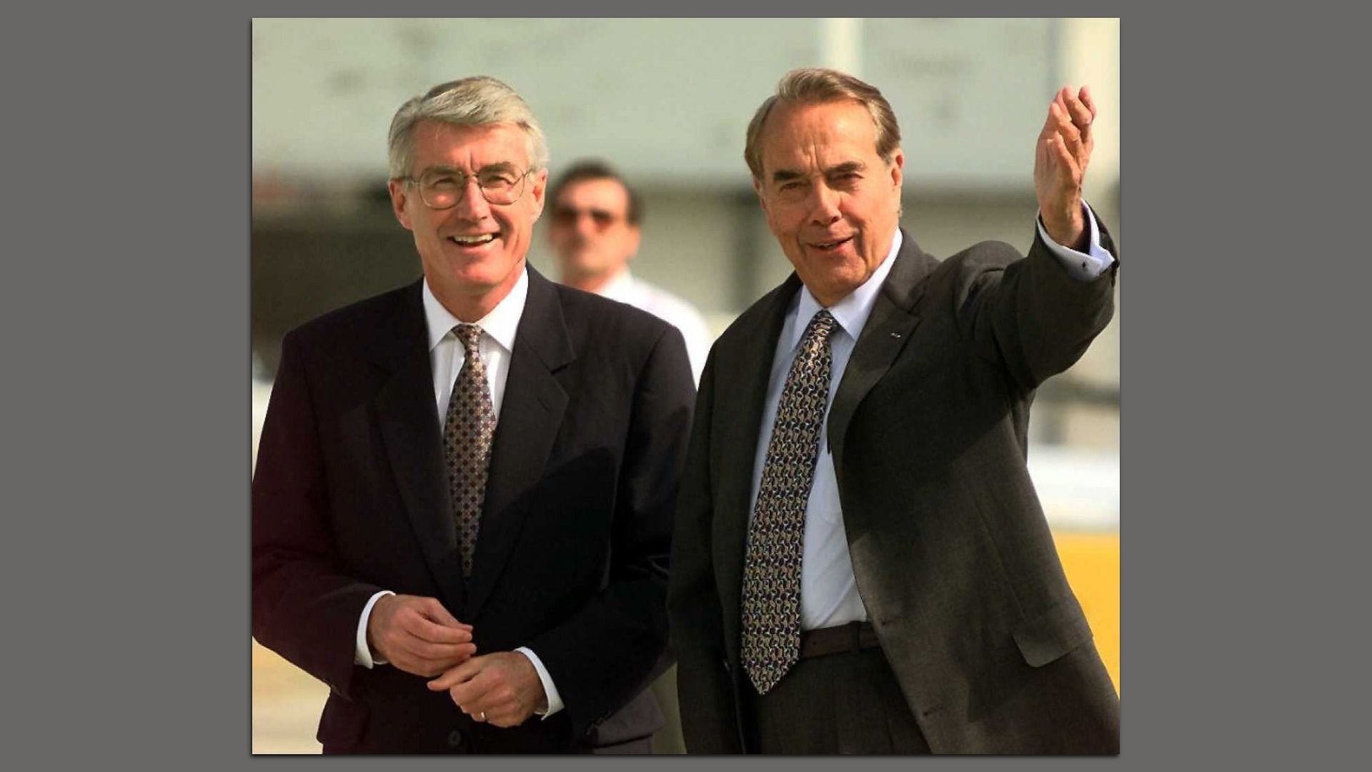 Photo of two men in suits waving to a crowd. 