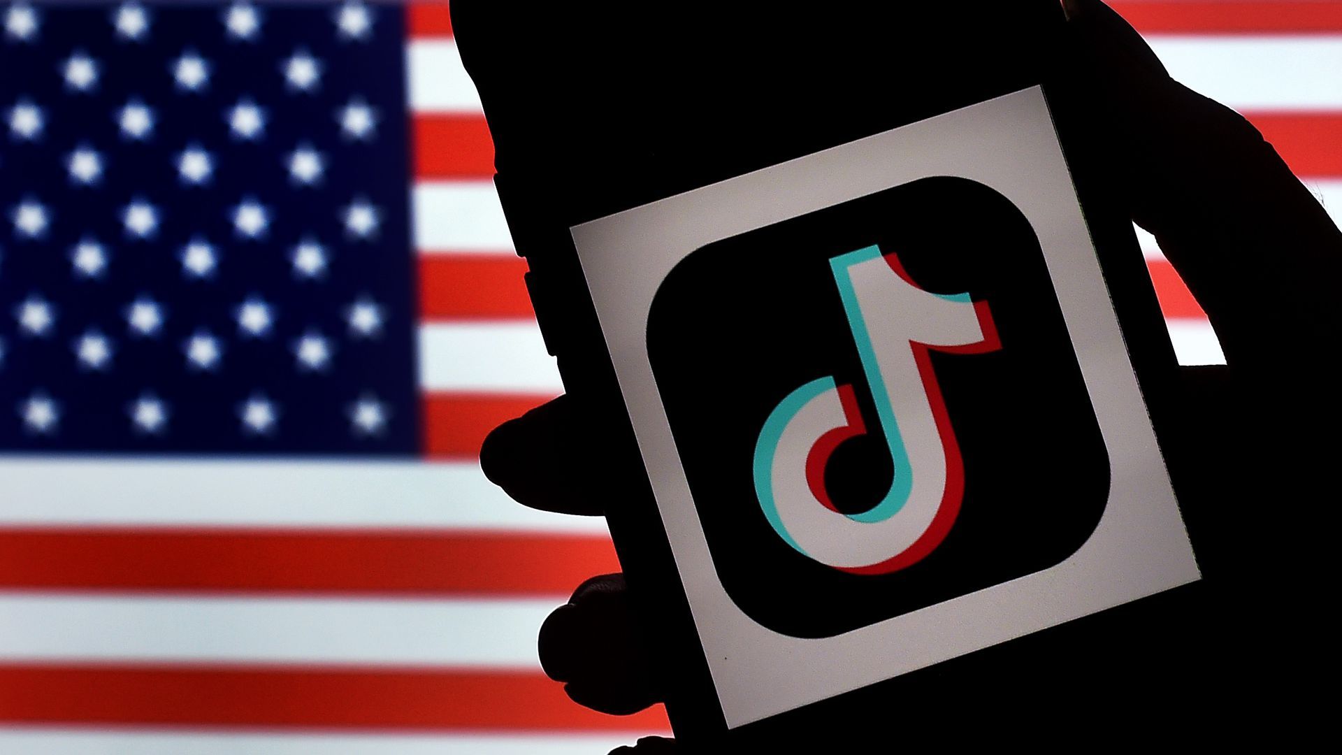 An illustration shows a smartphone bearing a TikTok logo set against the backdrop of an American flag.