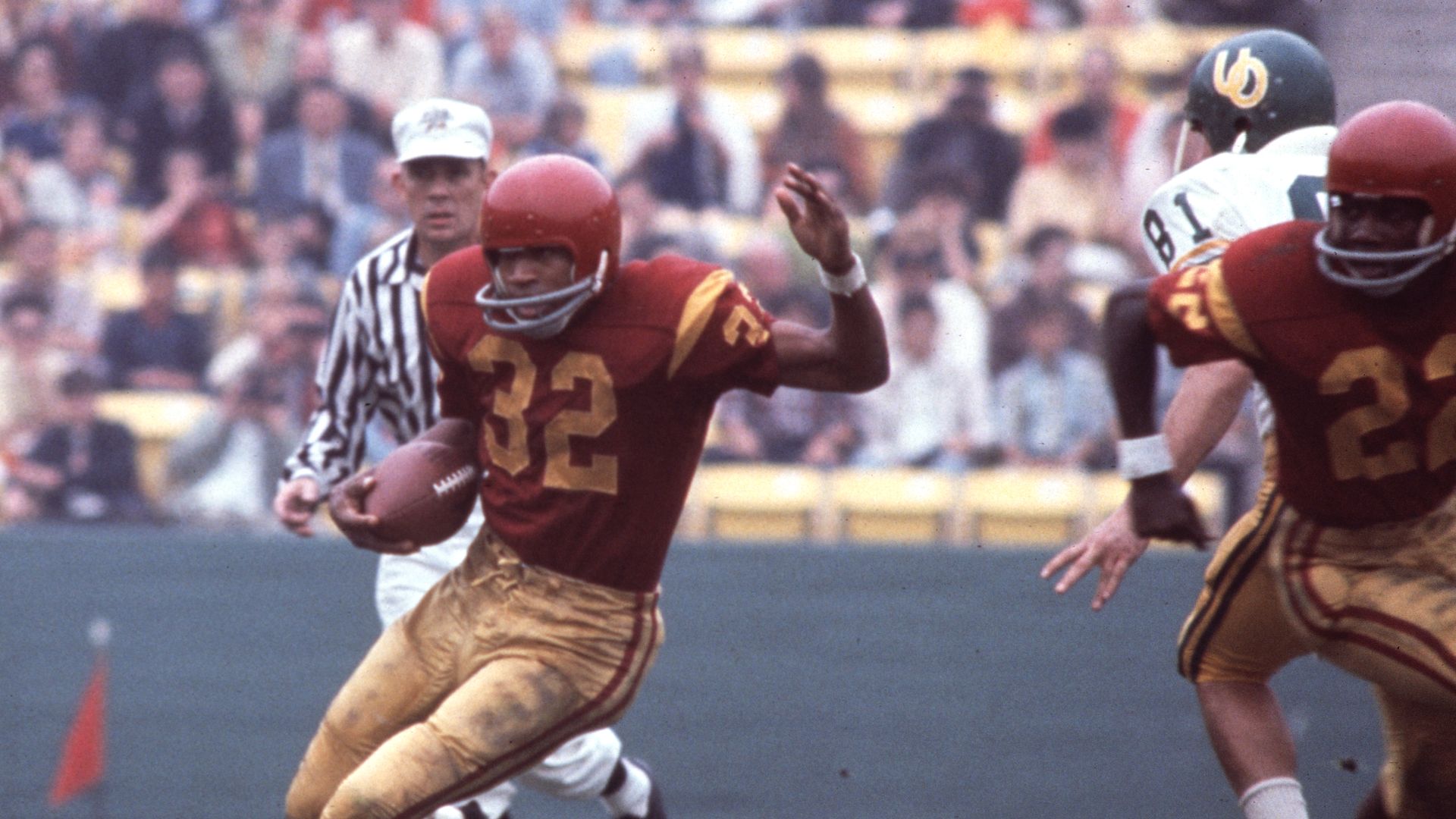 A man wearing No. 32 running the football in a red and yellow uniform