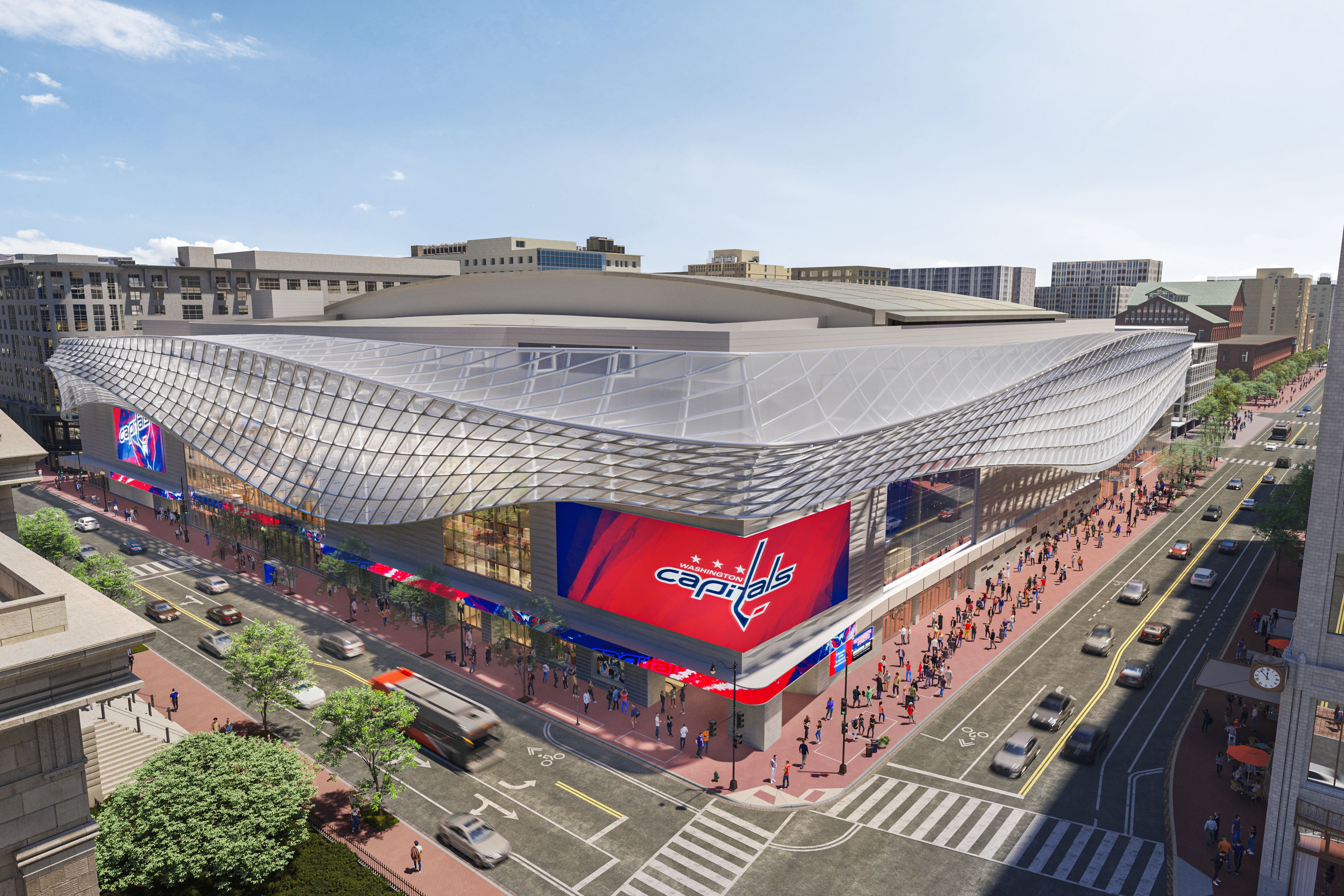 Modern arena with wave-like glass roof and large red Washington Capitals logo screens, surrounded by city streets with cars, buses, and crowds on sidewalks under a clear blue sky.