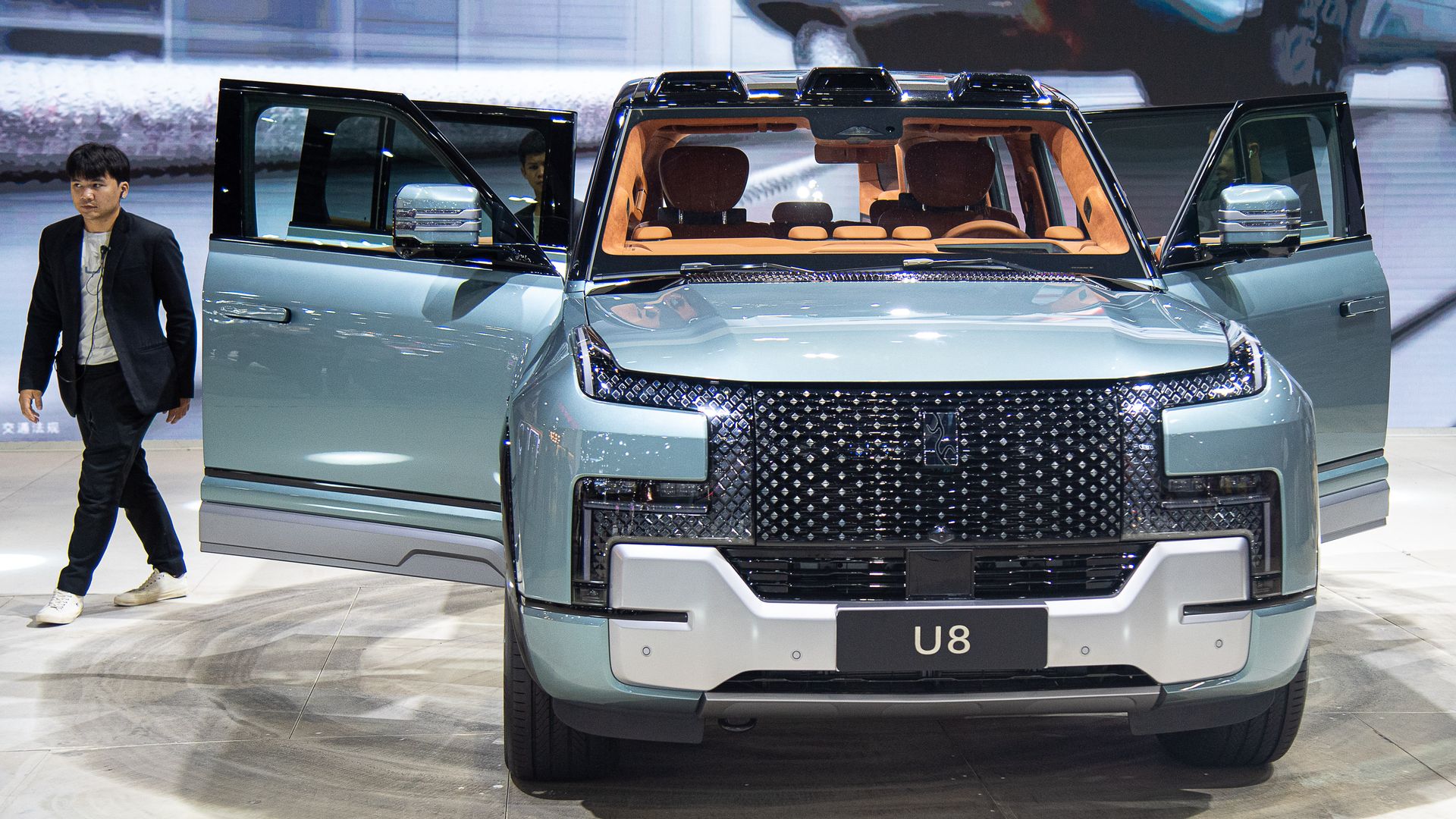 A light-turquoise colored vehicle sits in a display area of an auto show with its front doors open