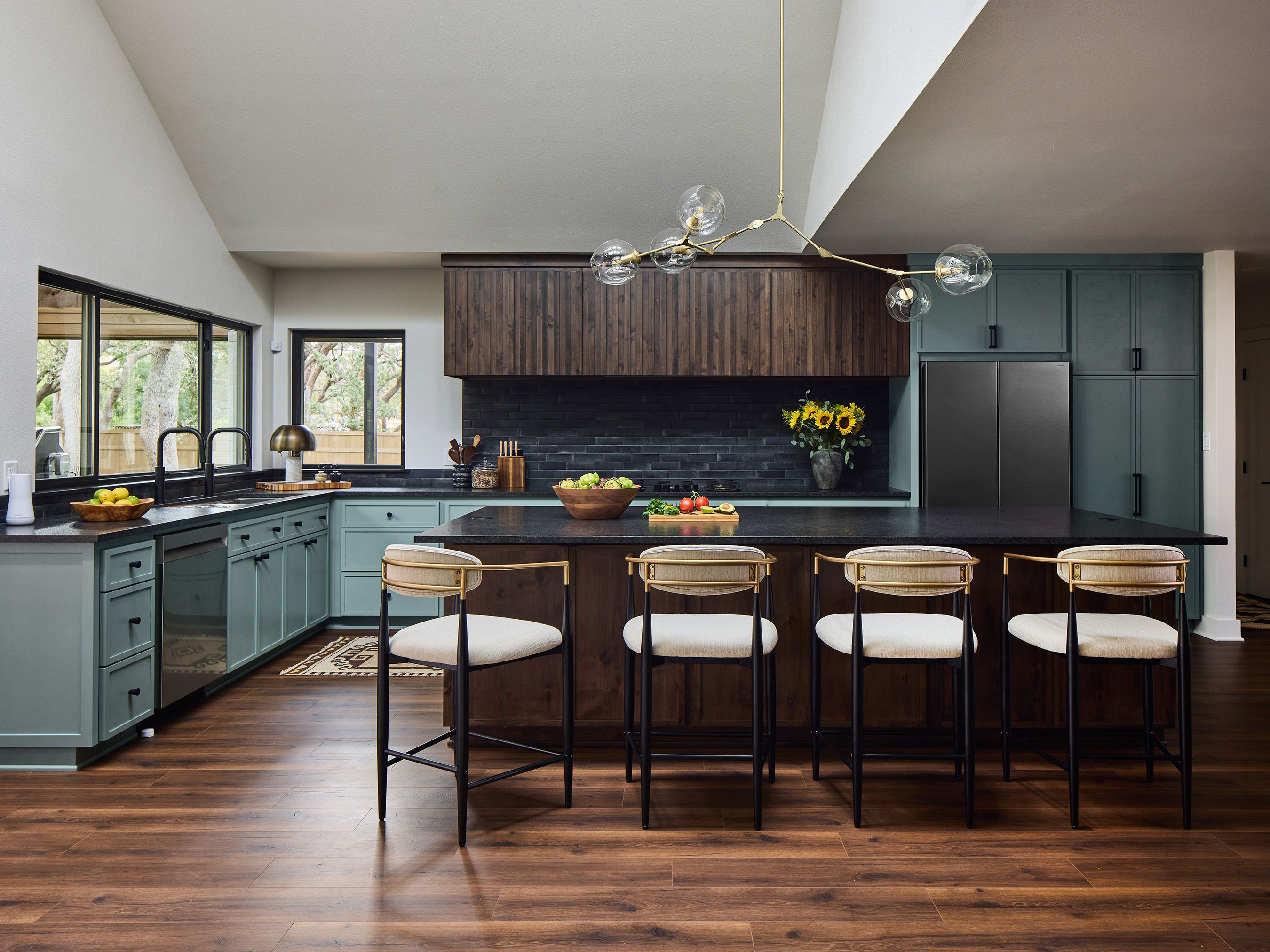 A kitchen features blue cabinets, gray wall tile and four barstools at the island.