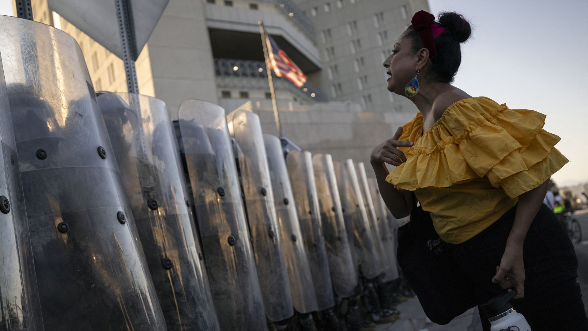 Woman in yellow shirt in front of line of troops with shields