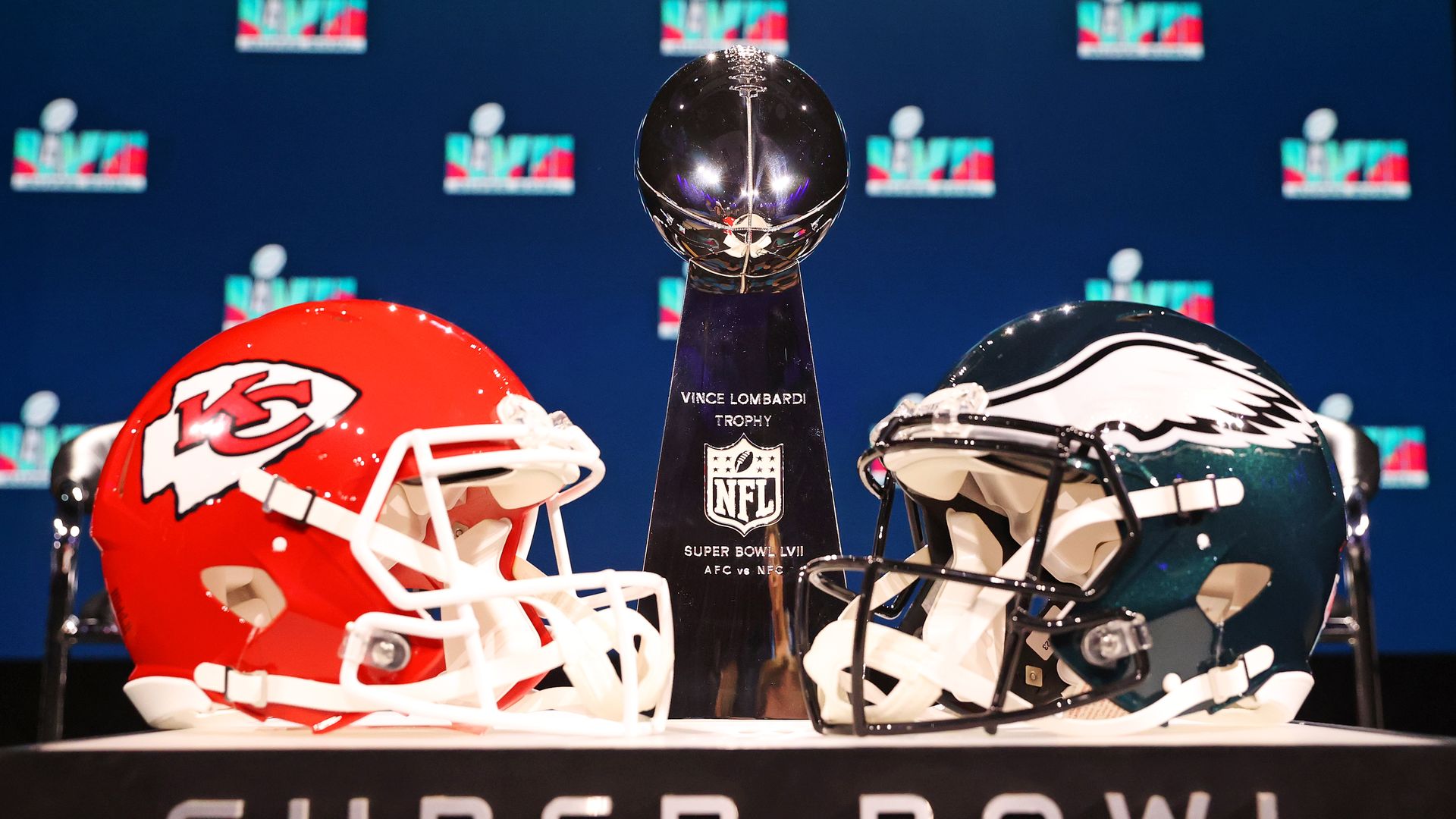 A red NFL helmet, the super bowl trophy and a blue helmet sit on a table