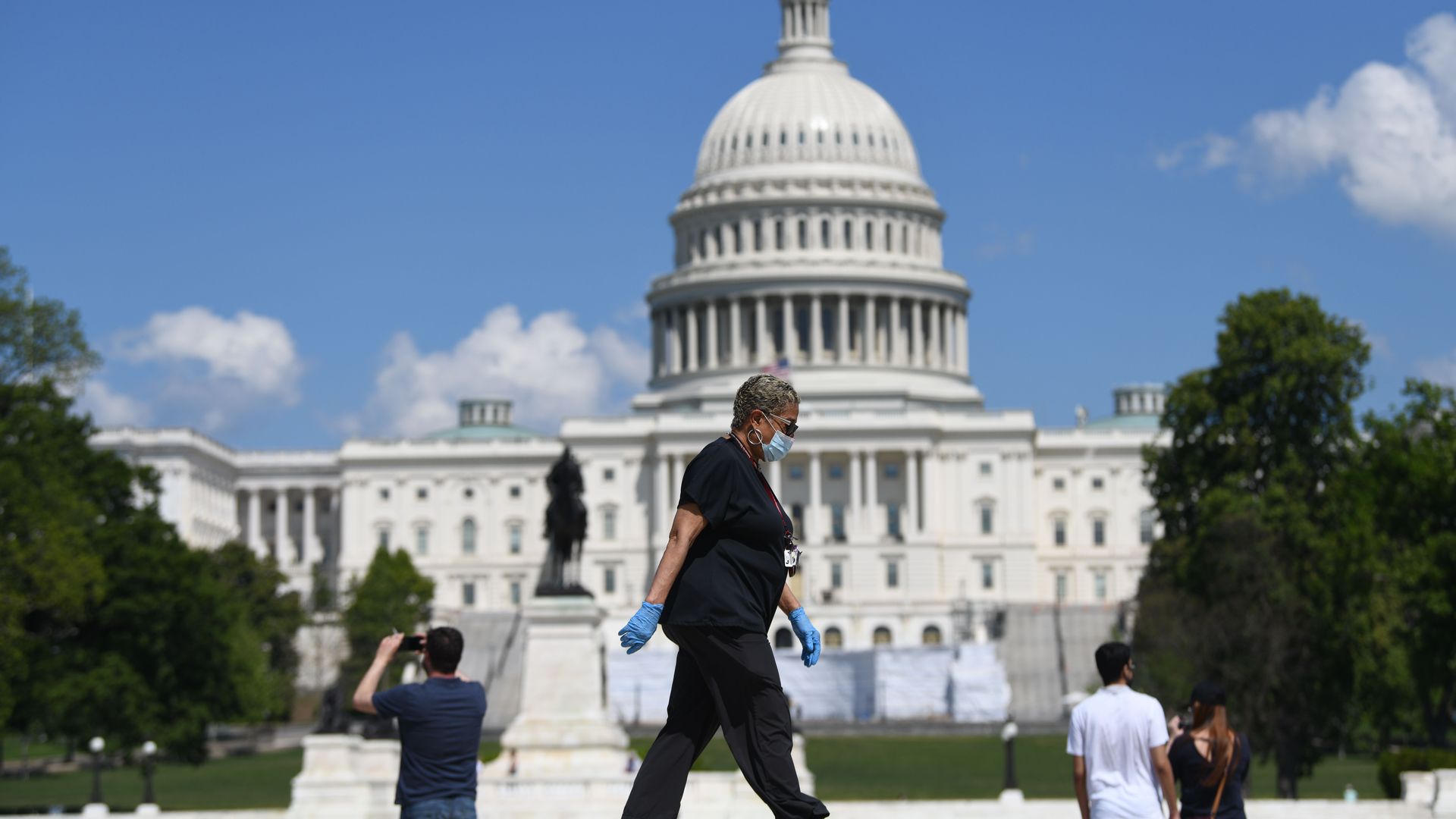 A woman wearing gloves and a face masks walking in front of the U.S. Capitol building