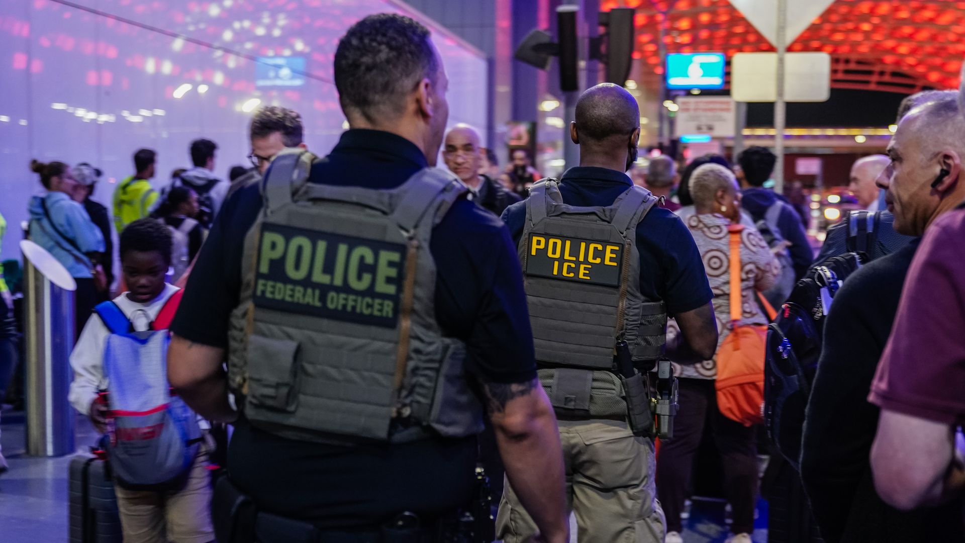 Travelers queue at an airport security checkpoint in Atlanta while uniformed ICE and federal officers stand nearby.
