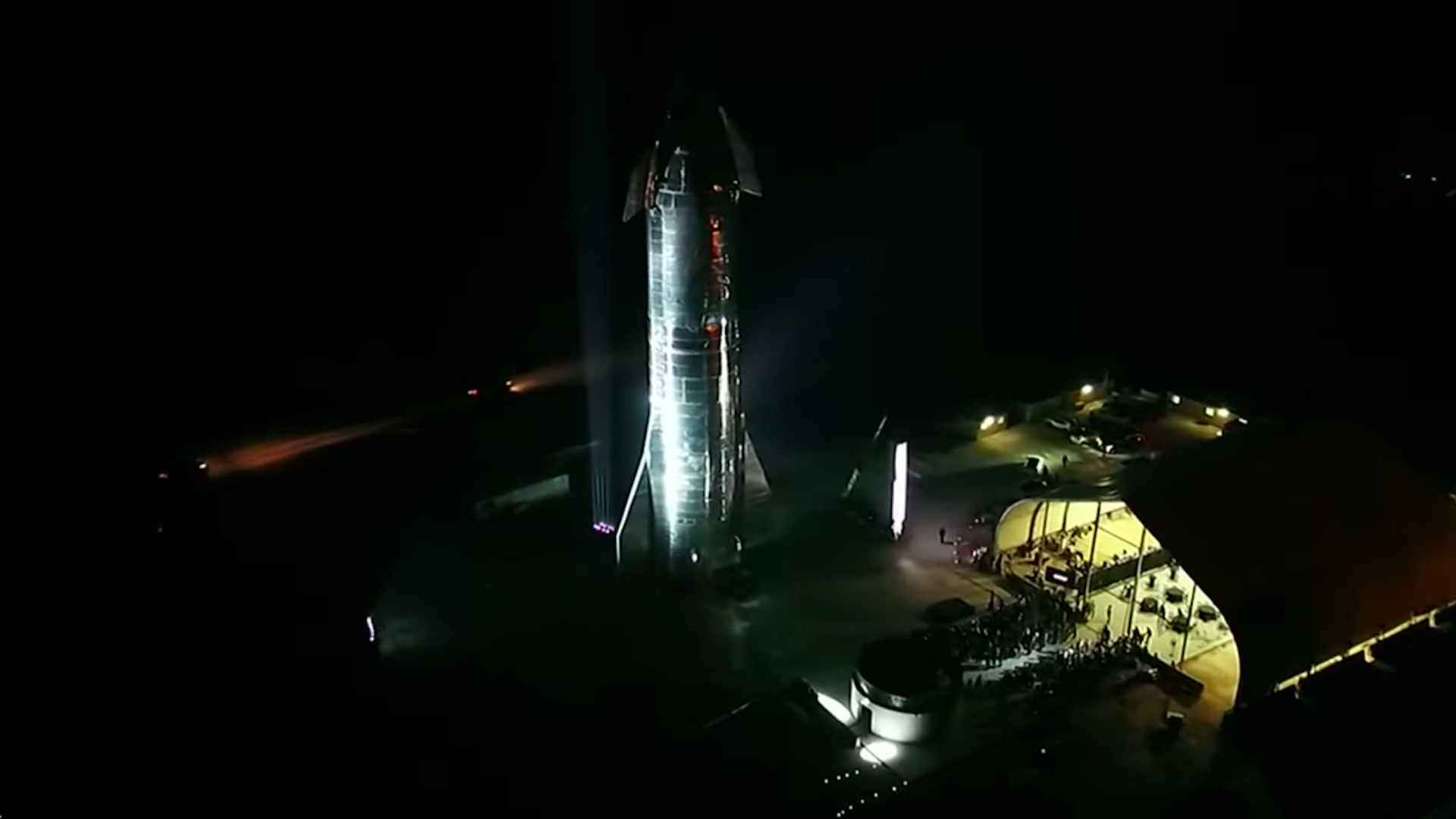 A prototype Starship in silver standing in Boca Chica, Texas at night