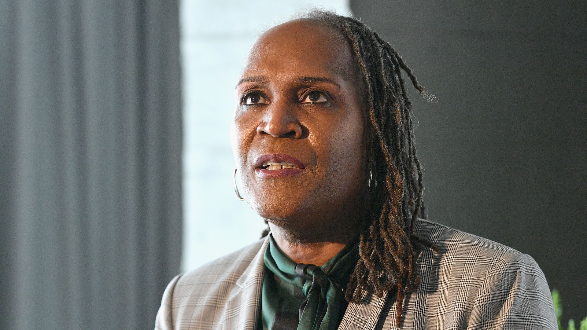A woman with dark skin and short locks in a business suit sits and speaks during a panel discussion