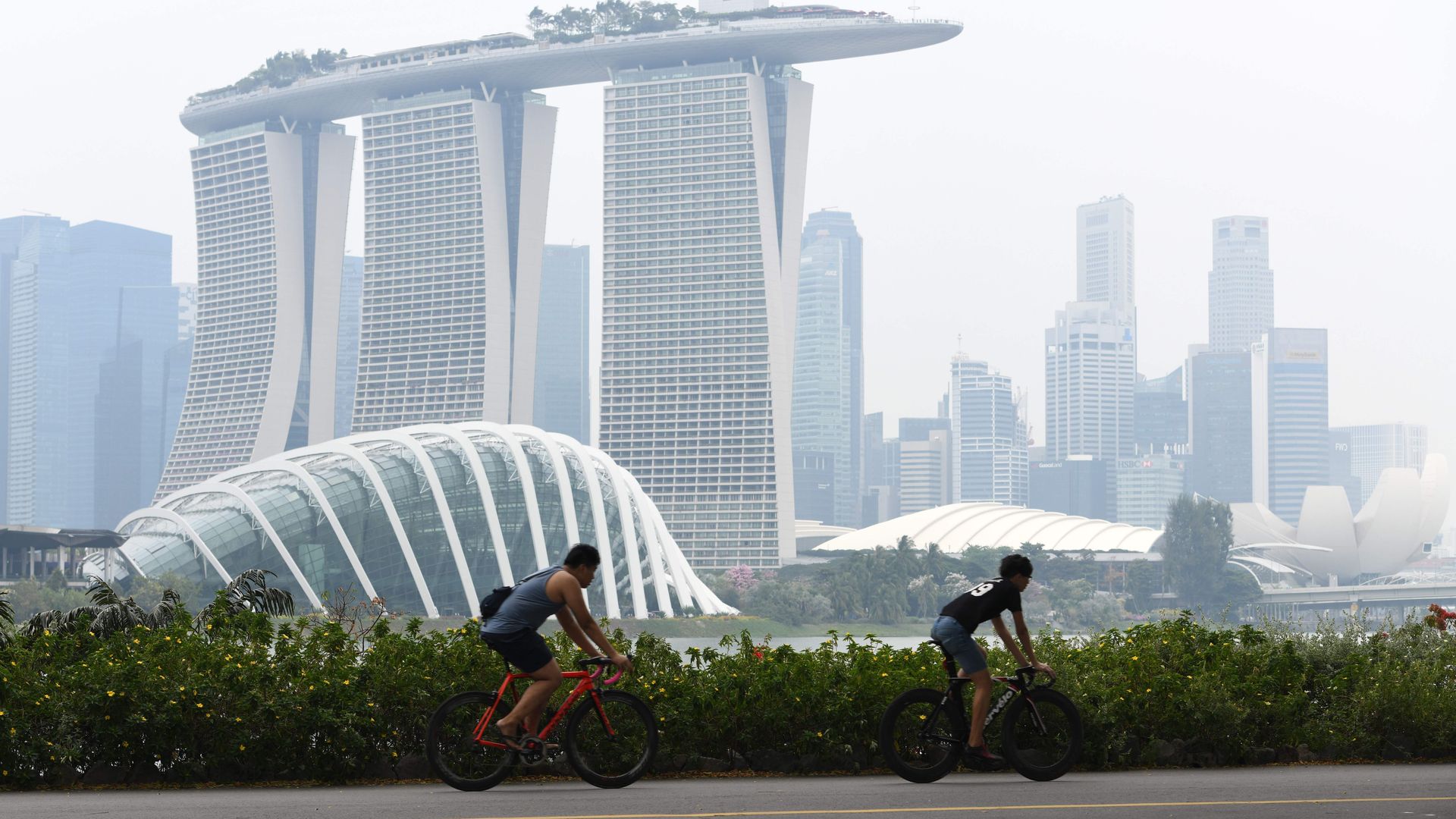 People cycle before the city skyline on a hazy day in Singapore 