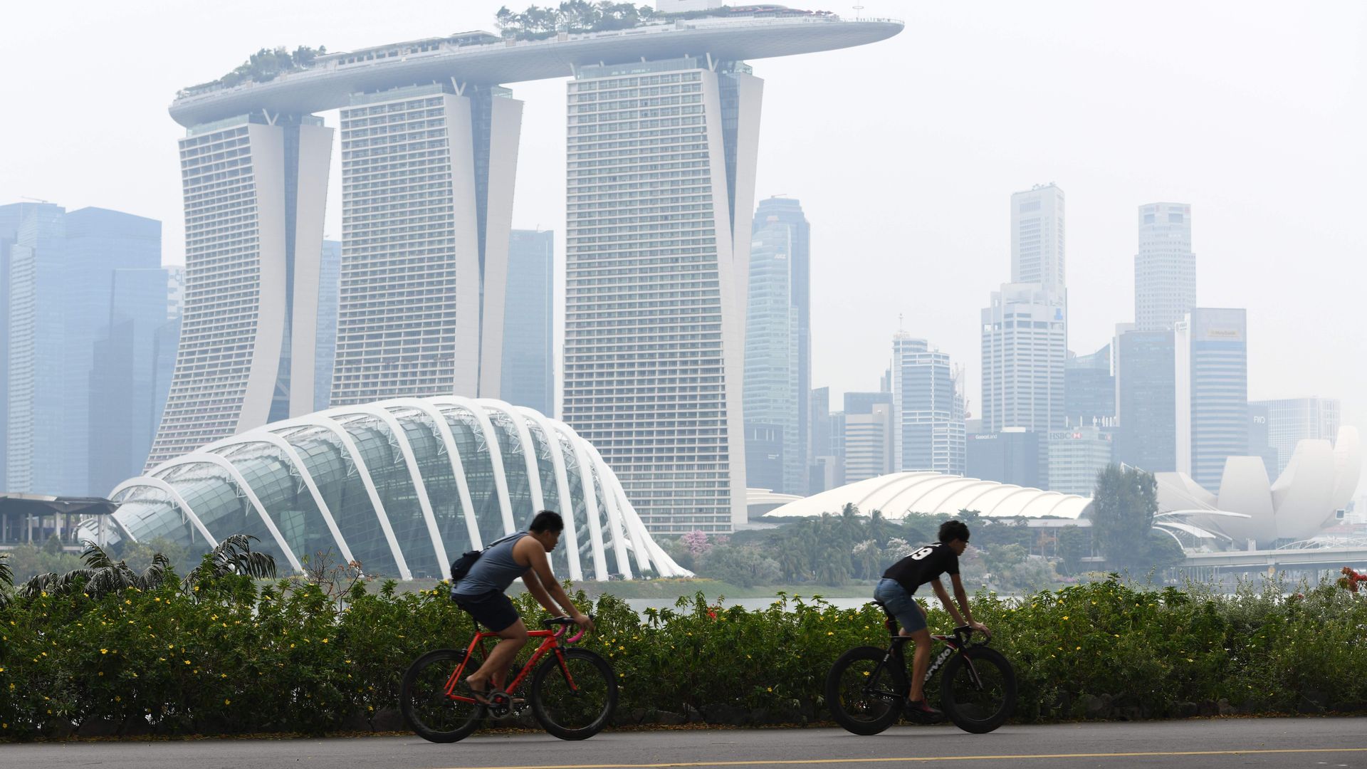 People cycle before the city skyline on a hazy day in Singapore