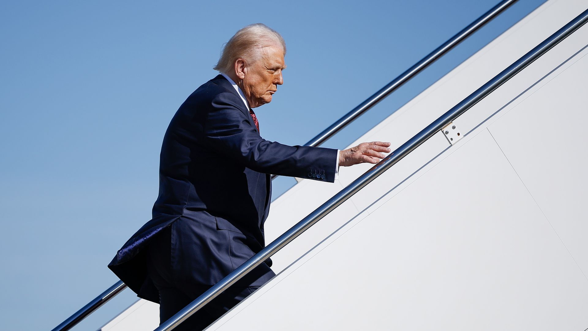 Trump ascends stairs with a blue sky in the background