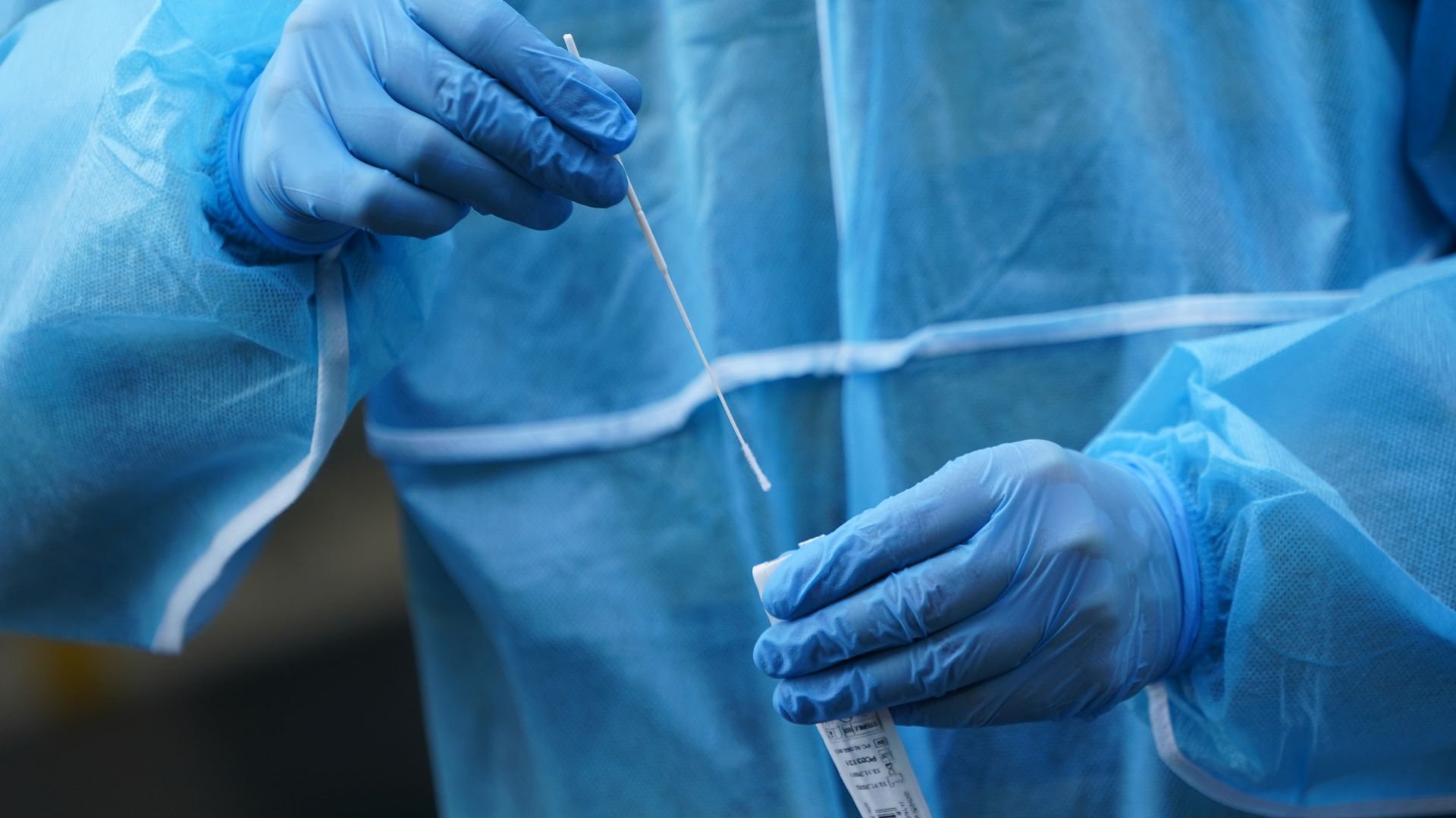 A medical worker dressed in PPE prepares to take a throat swab sample for a rapid antigen Covid test