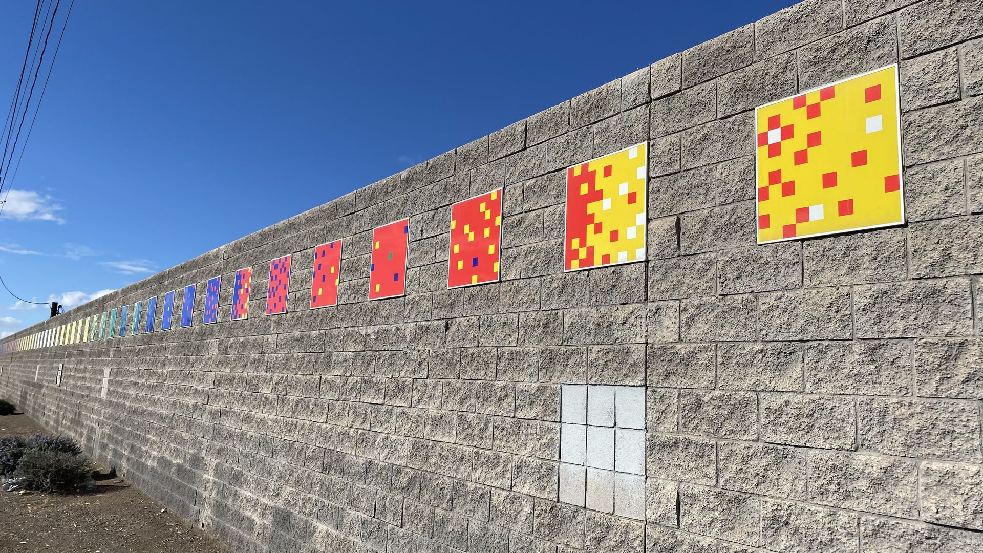 A gray brick wall with a long row of colored squares running horizontally near the top. 