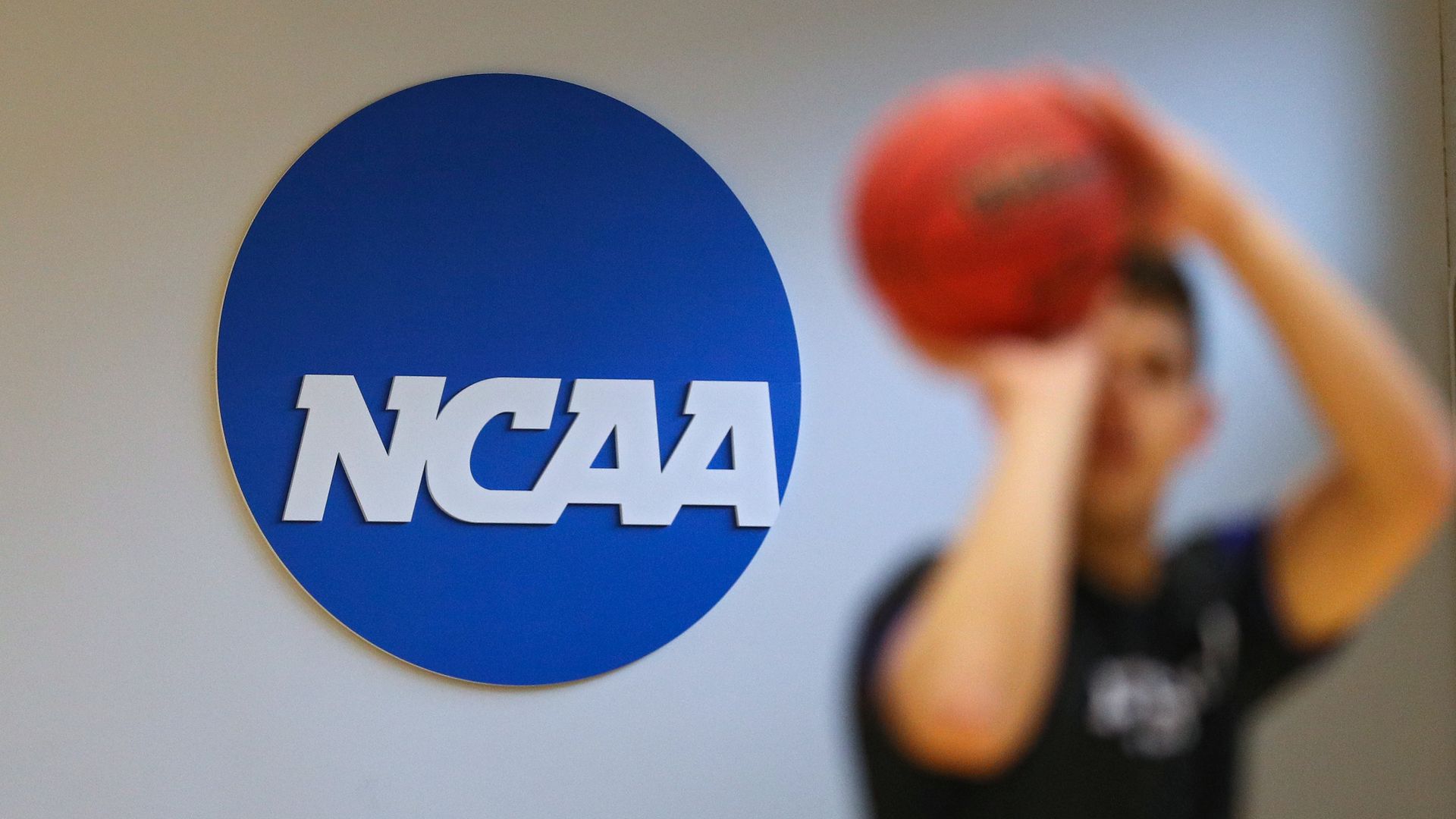 NCAA logo behind a student playing basketball