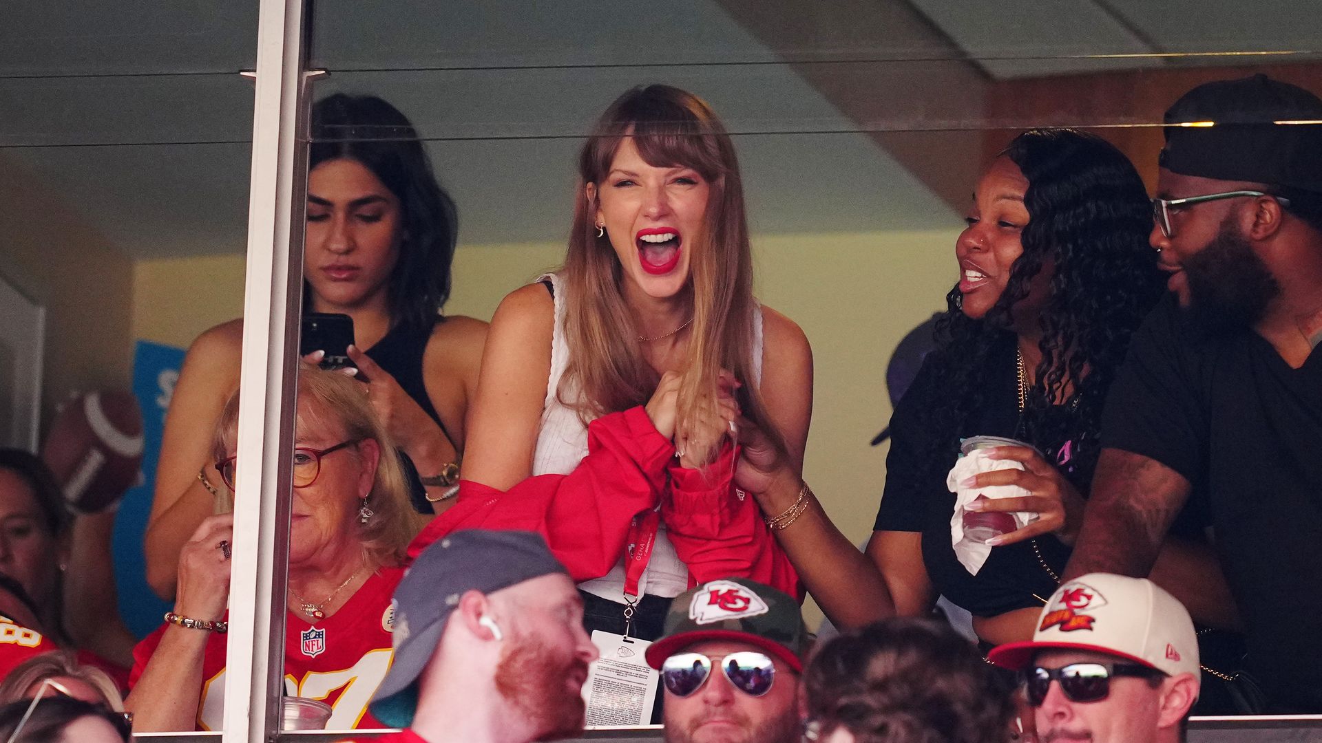 Taylor Swift cheers and laughs inside a vip box at a football game. 