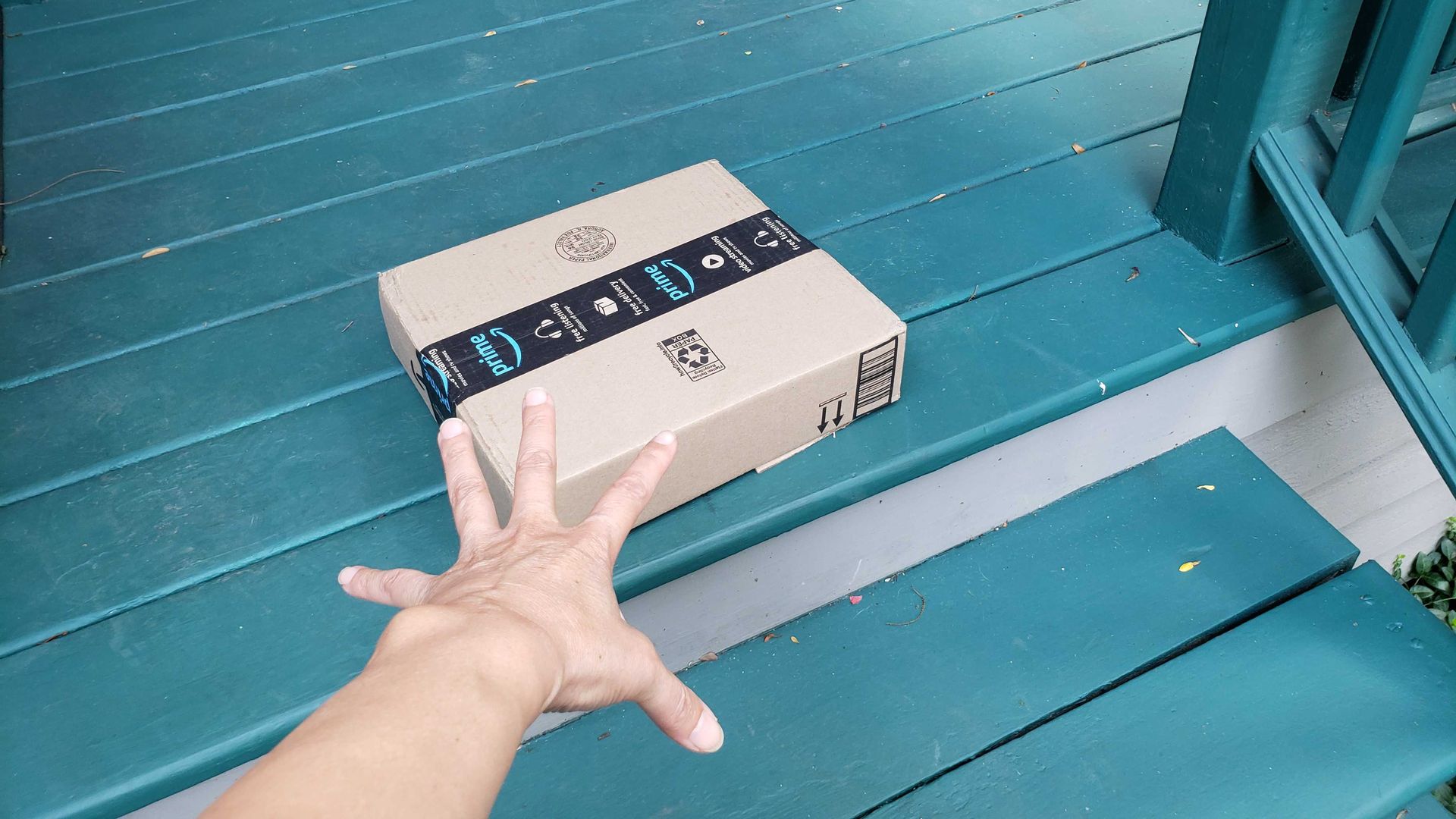 Hand reaching for Amazon box on a turquoise-colored wood porch.