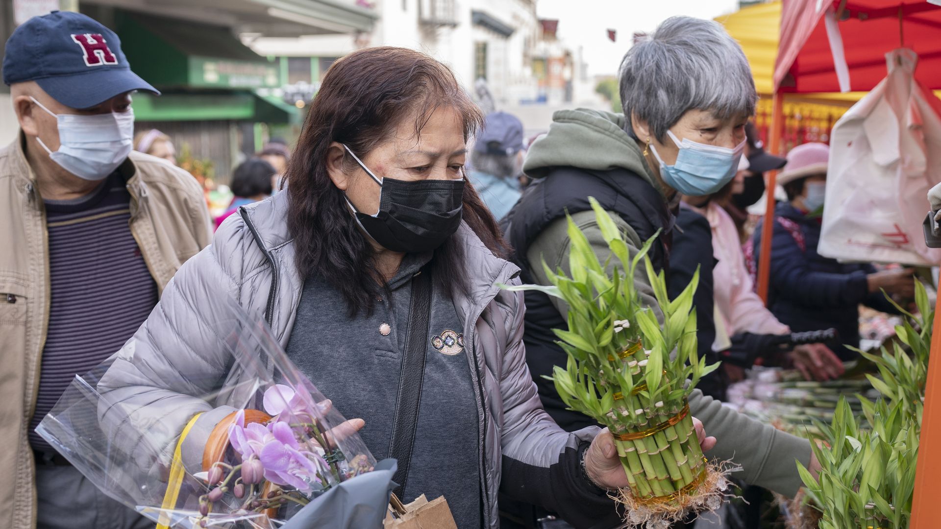 three people shop for flowers. person in front has two flowers in hand.