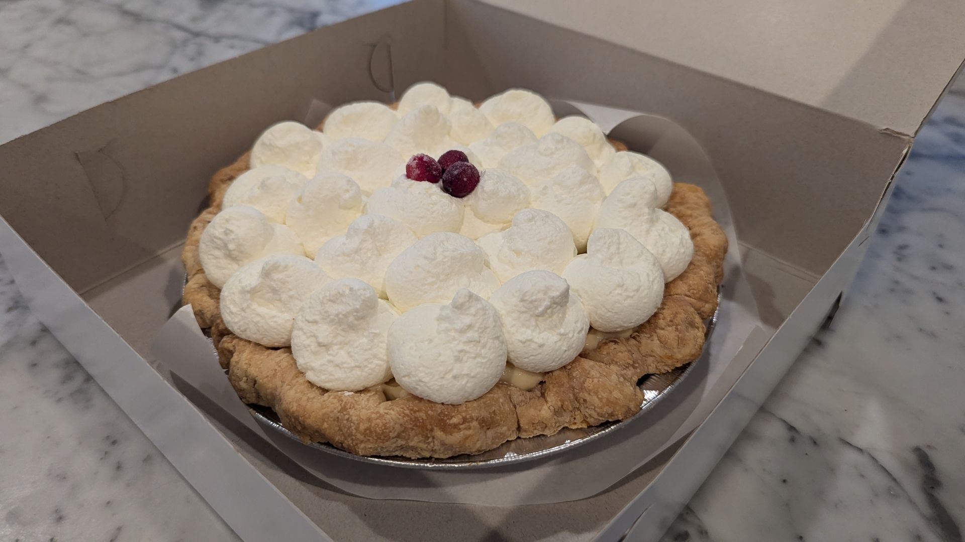 A full pie with blobs of whipped cream and cranberries.