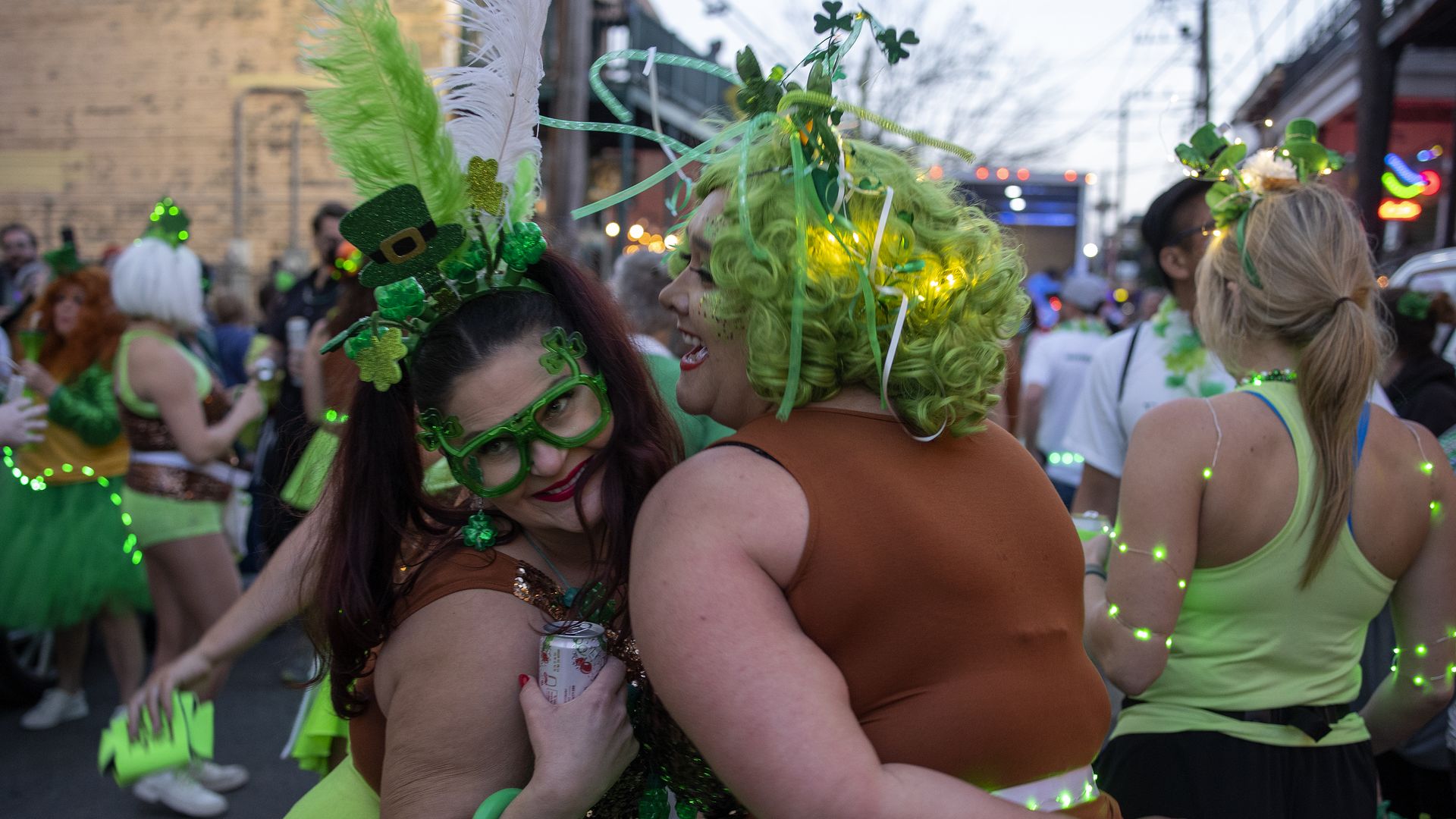 Two women speak closely to each other on a busy Marigny street. They wear green wigs and head-dresses.