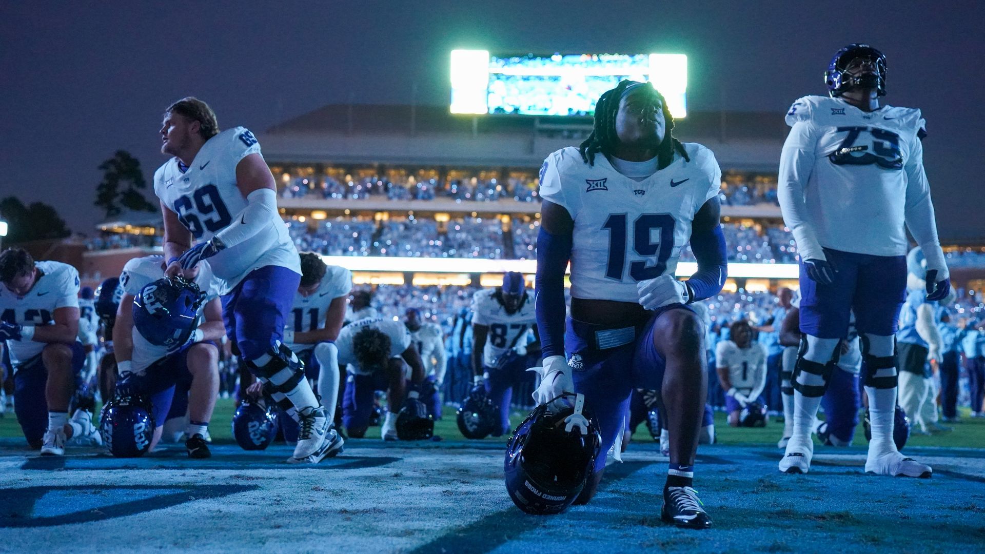 TCU football players take a knee on a field
