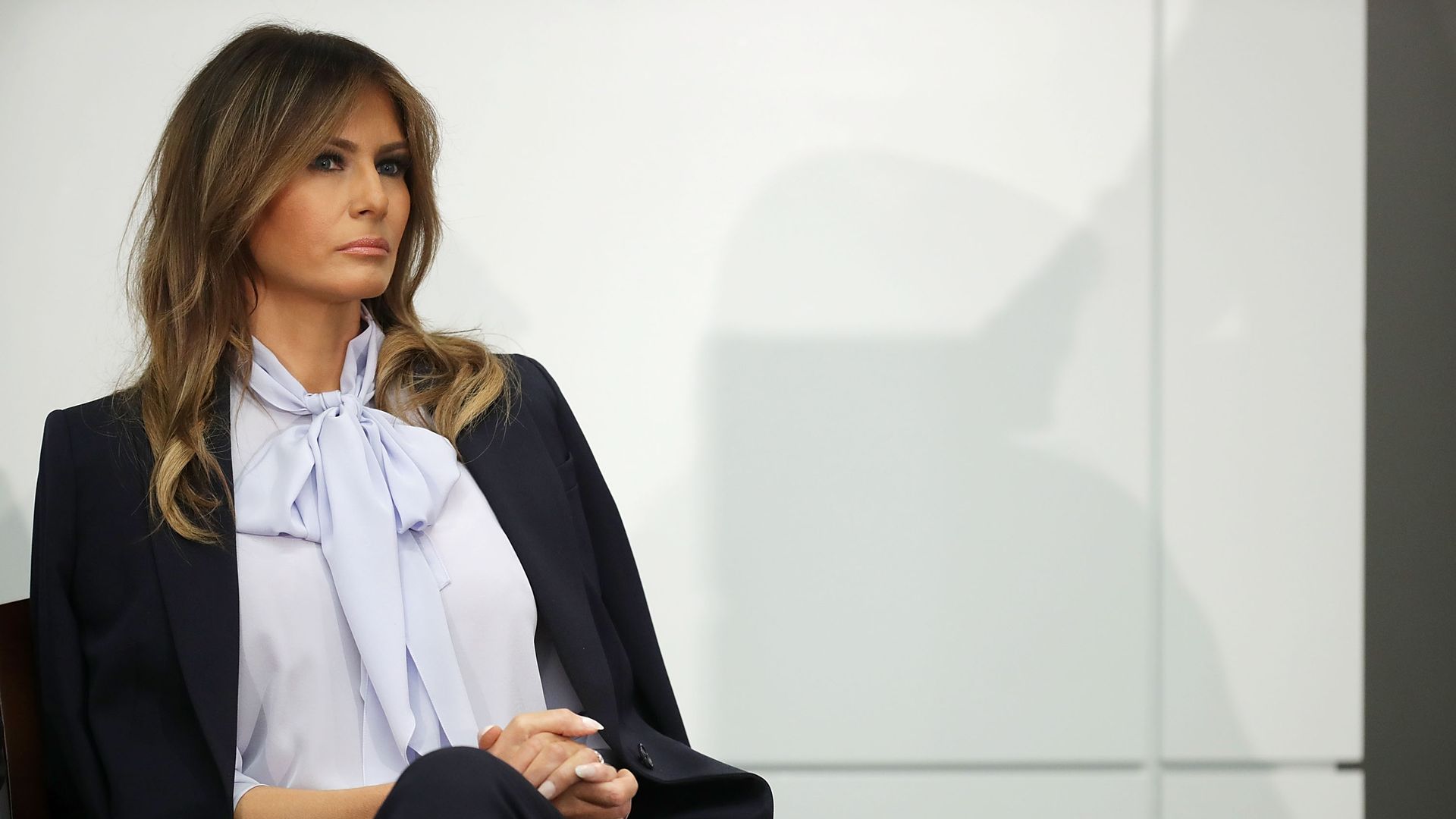 Melania Trump sitting in a chair on stage with a serious expression