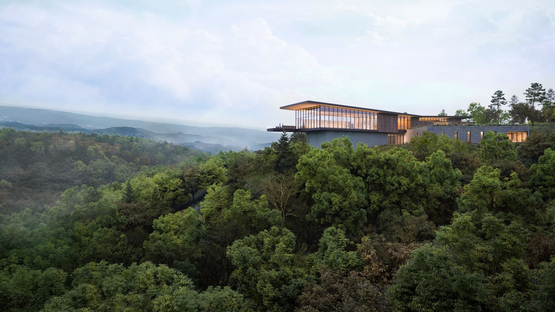 Modern glass-and-wood house sits on a cliff above a dense forest, with wide windows; distant blue mountains and a bright, partly cloudy sky completing the landscape.