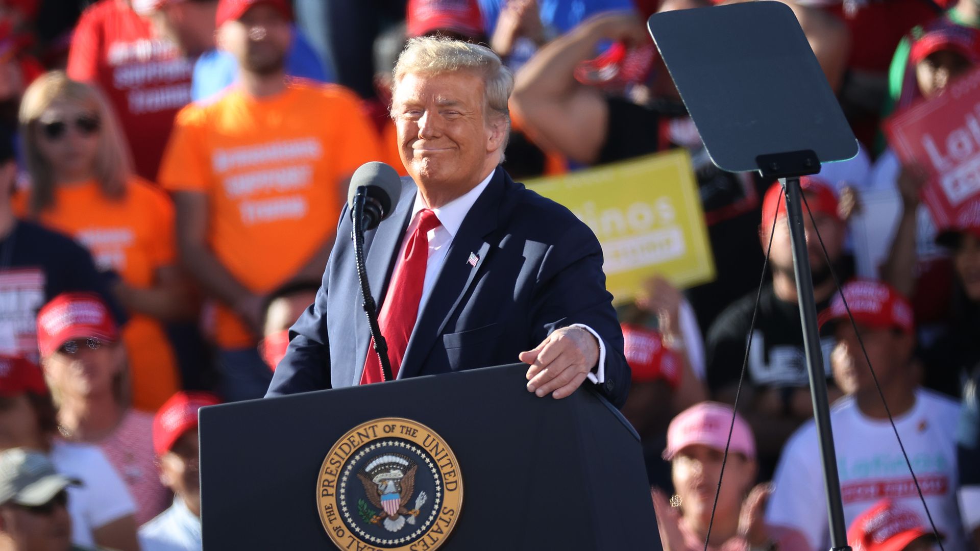 Photo of a smiling Donald Trump standing behind a podium at a Trump rally