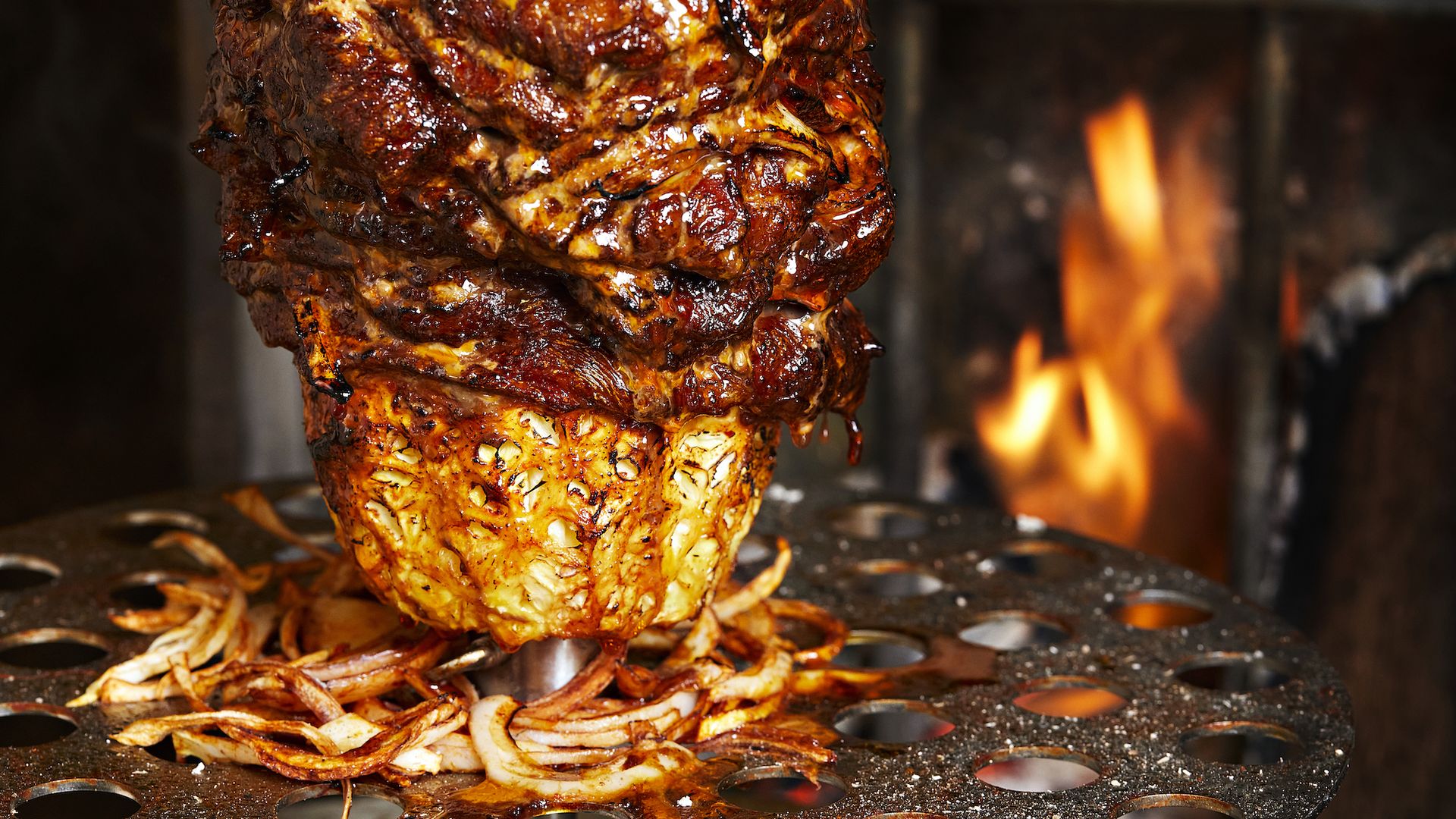 A spit with Mexican al pastor marinated pork sits above a flame