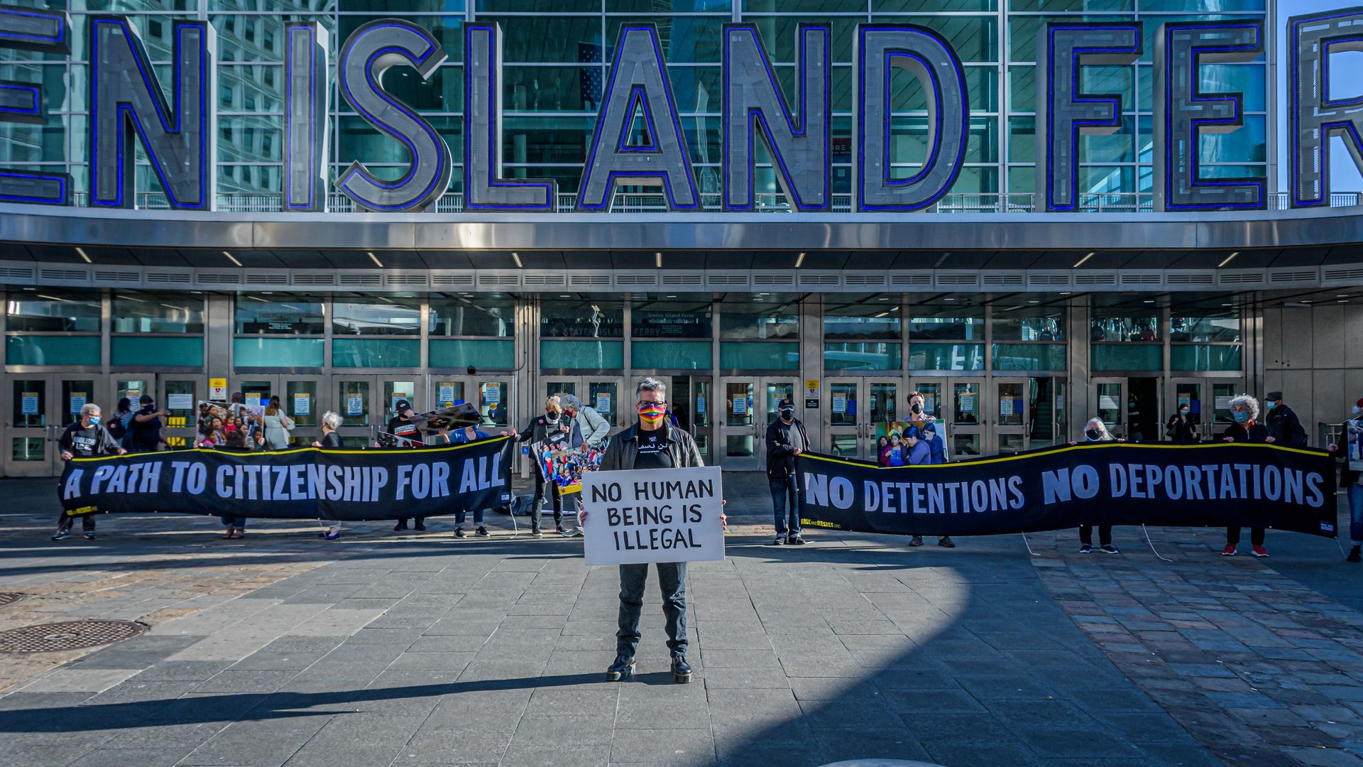 Photo of protesters with signs that read "A path to citizenship for all," "No human is illegal," and "No detentions, no deportations"