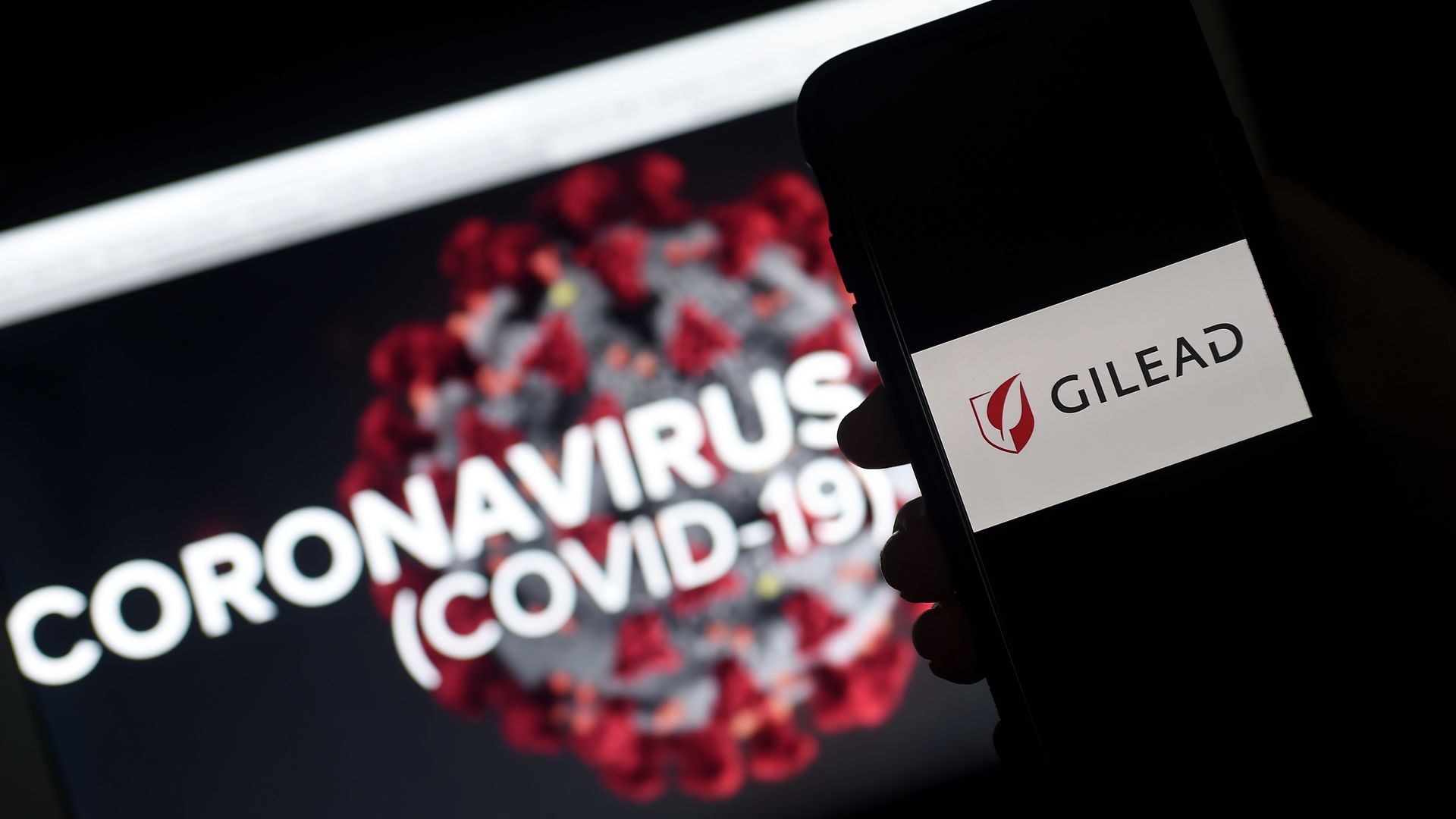 Gilead logo is displayed on a smartphone next to a screen showing a coronavirus graphic on March 25