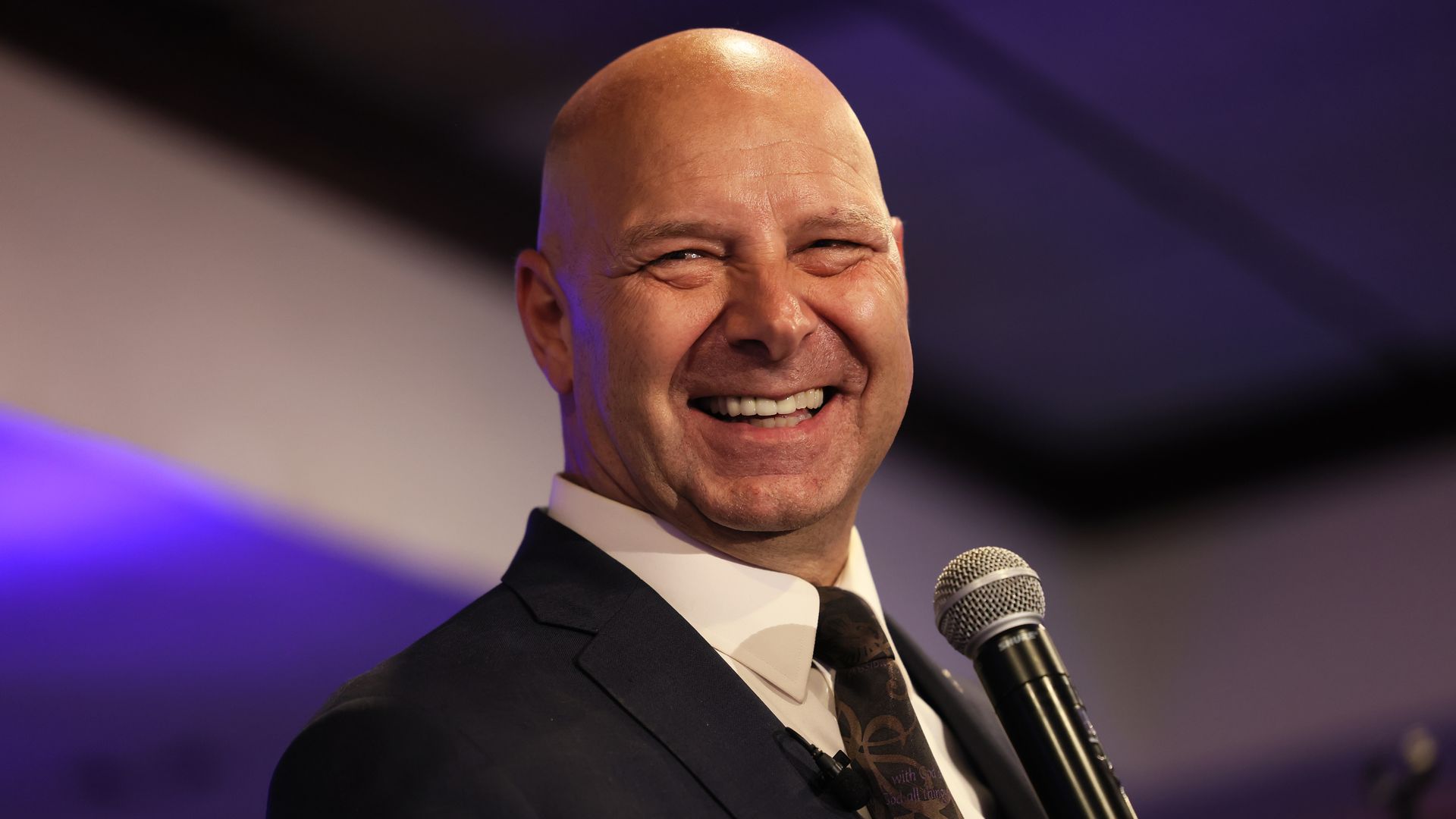 Doug Mastriano smiles while holding a microphone.